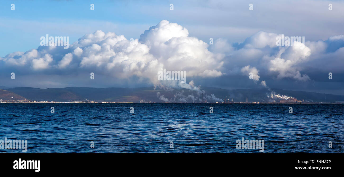 Port talbot steelworks viewed across the sea from the mumbles wales UK showing industrial pollution mixing with clouds Stock Photo