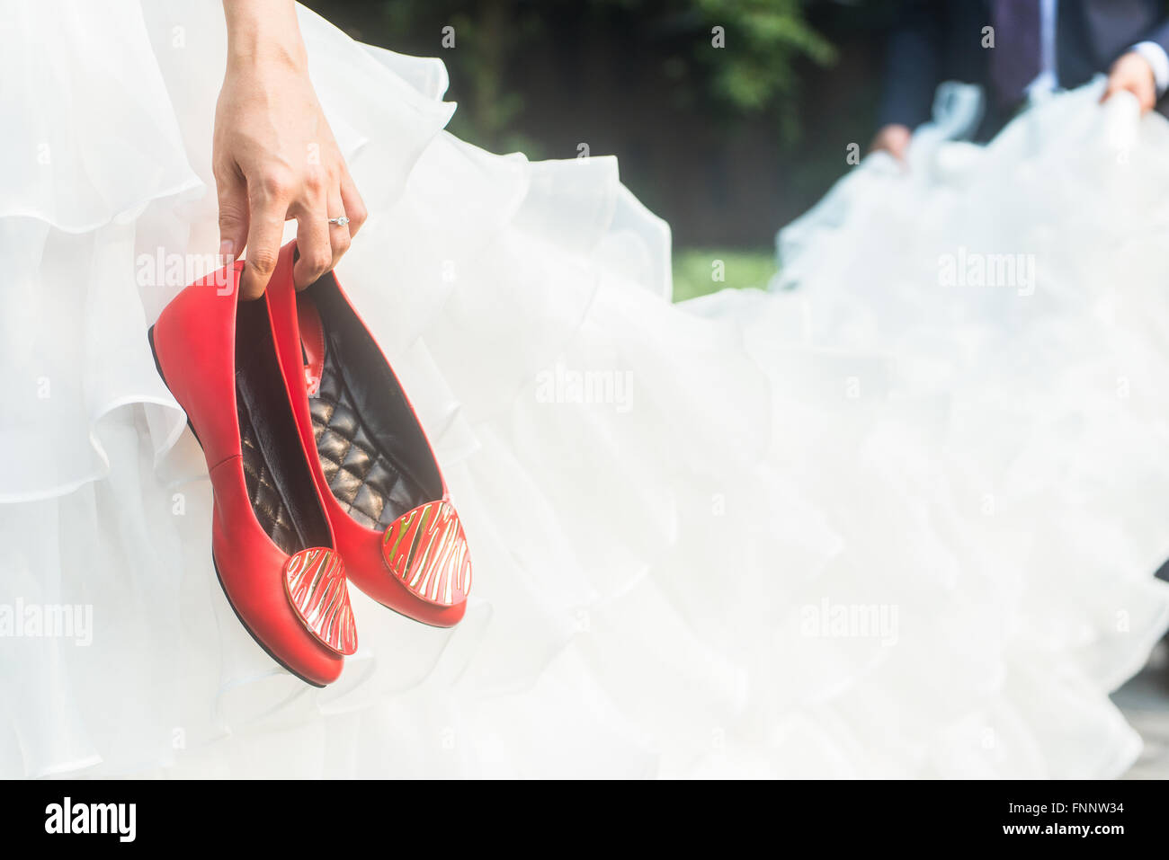 bride holding red shoes and groom holding the skirt Stock Photo