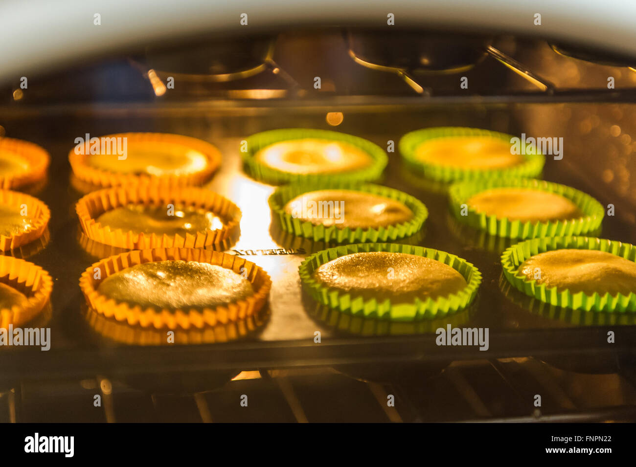 Cup cakes on a baking tray rise in the oven in a home kitchen. Stock Photo
