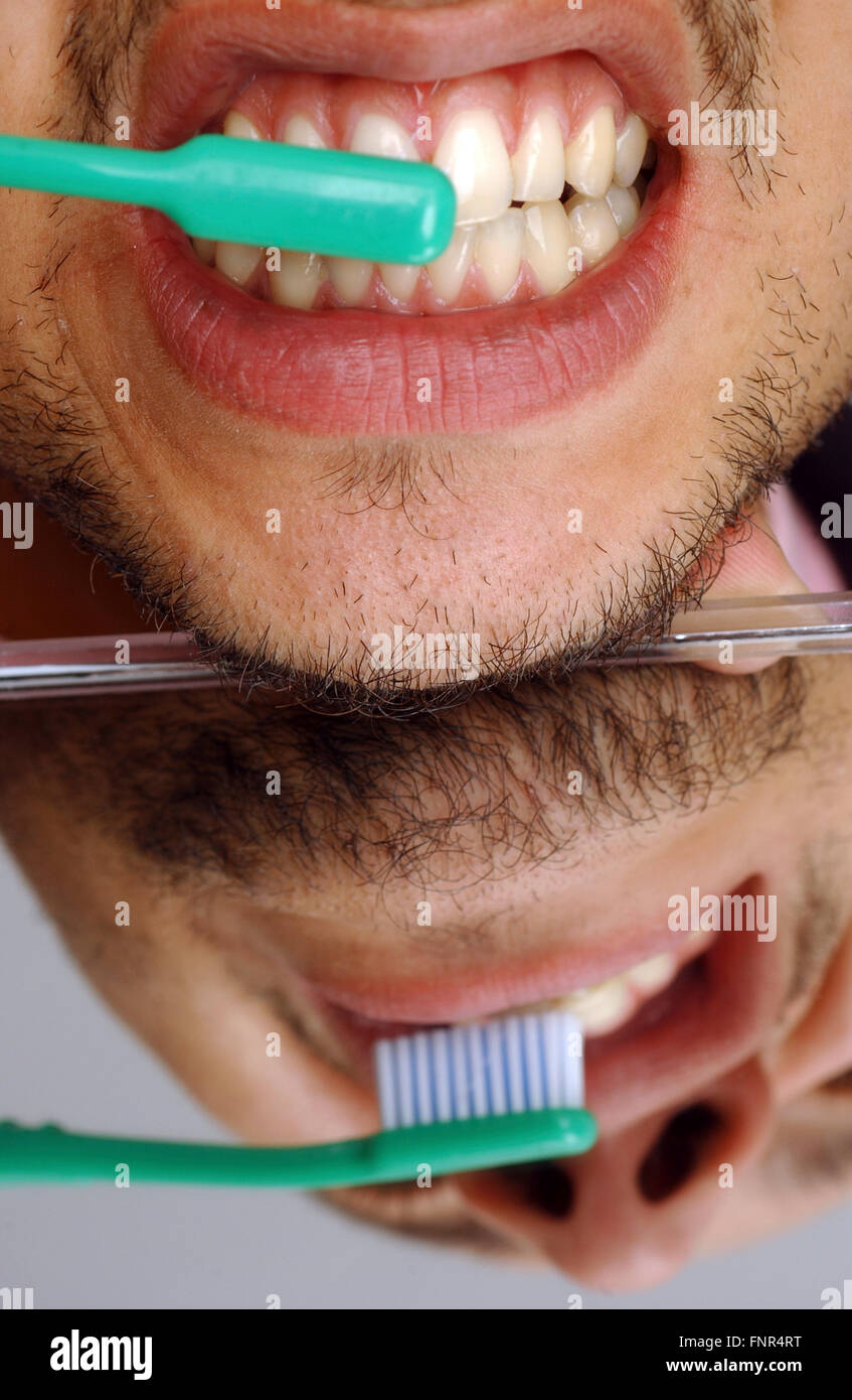 A young man brushing his teeth with toothpaste. Regular brushing of teeth helps prevent tooth decay and gum disease. Stock Photo