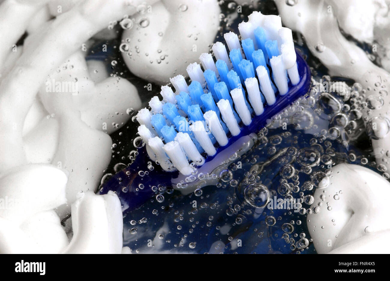 A blue toothbrush lying in a pool of toothpaste and water. Stock Photo