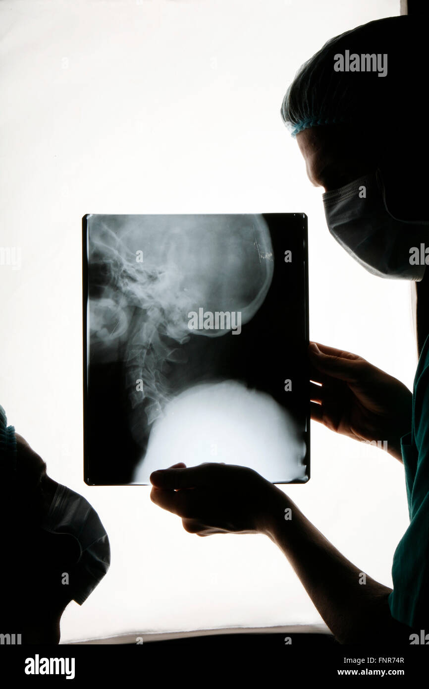 Surgeons examining a patient's x-ray of her upper back and neck prior to surgery. Stock Photo