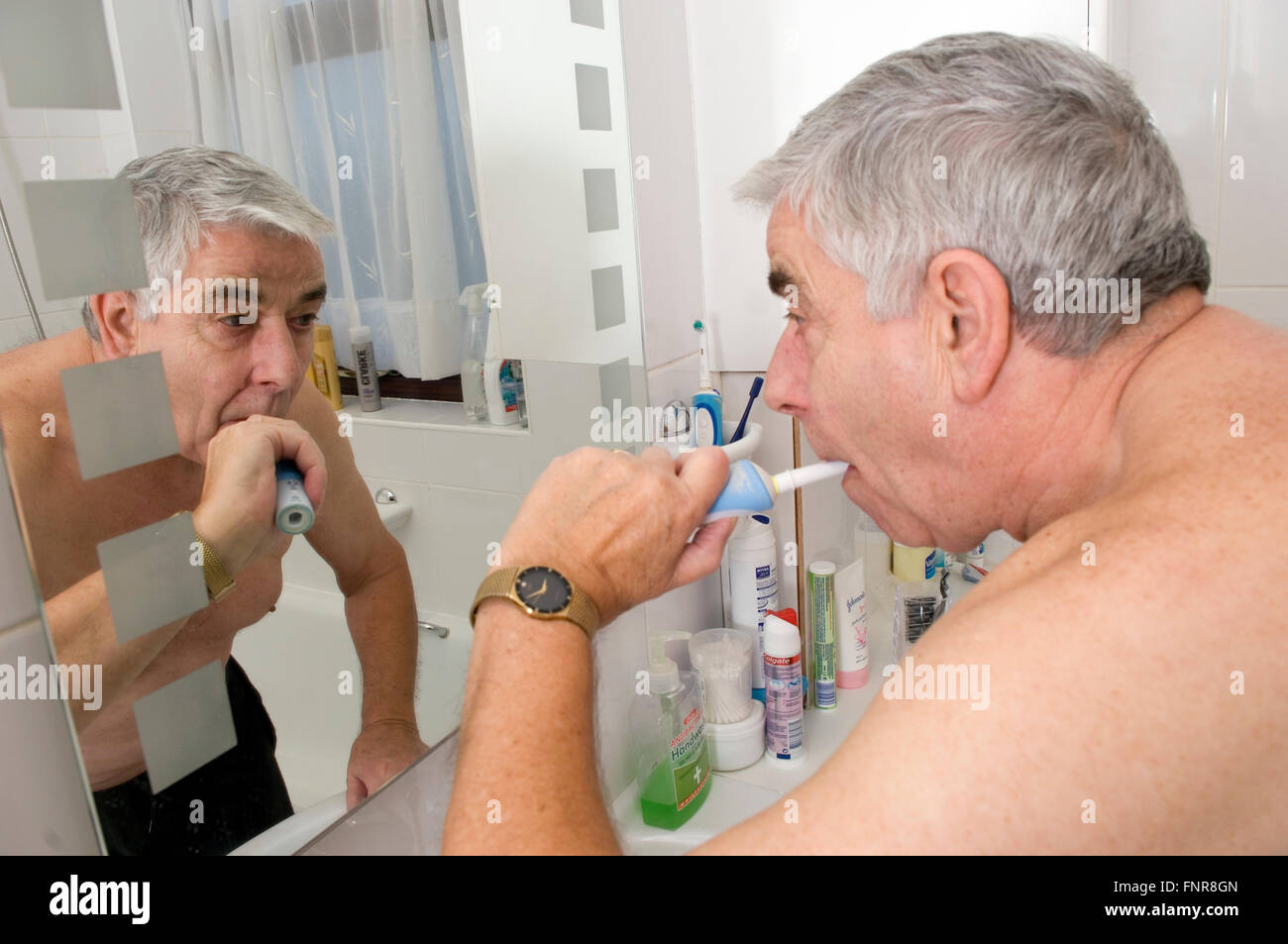 Elderly Man brushing his teeth using an electric toothbrush. Stock Photo