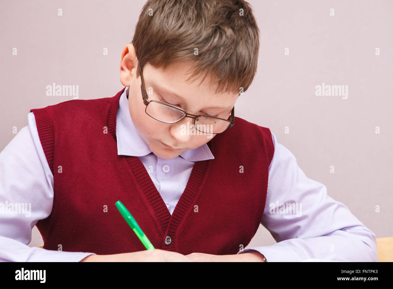 boy with glasses sitting at a desk writing Stock Photo