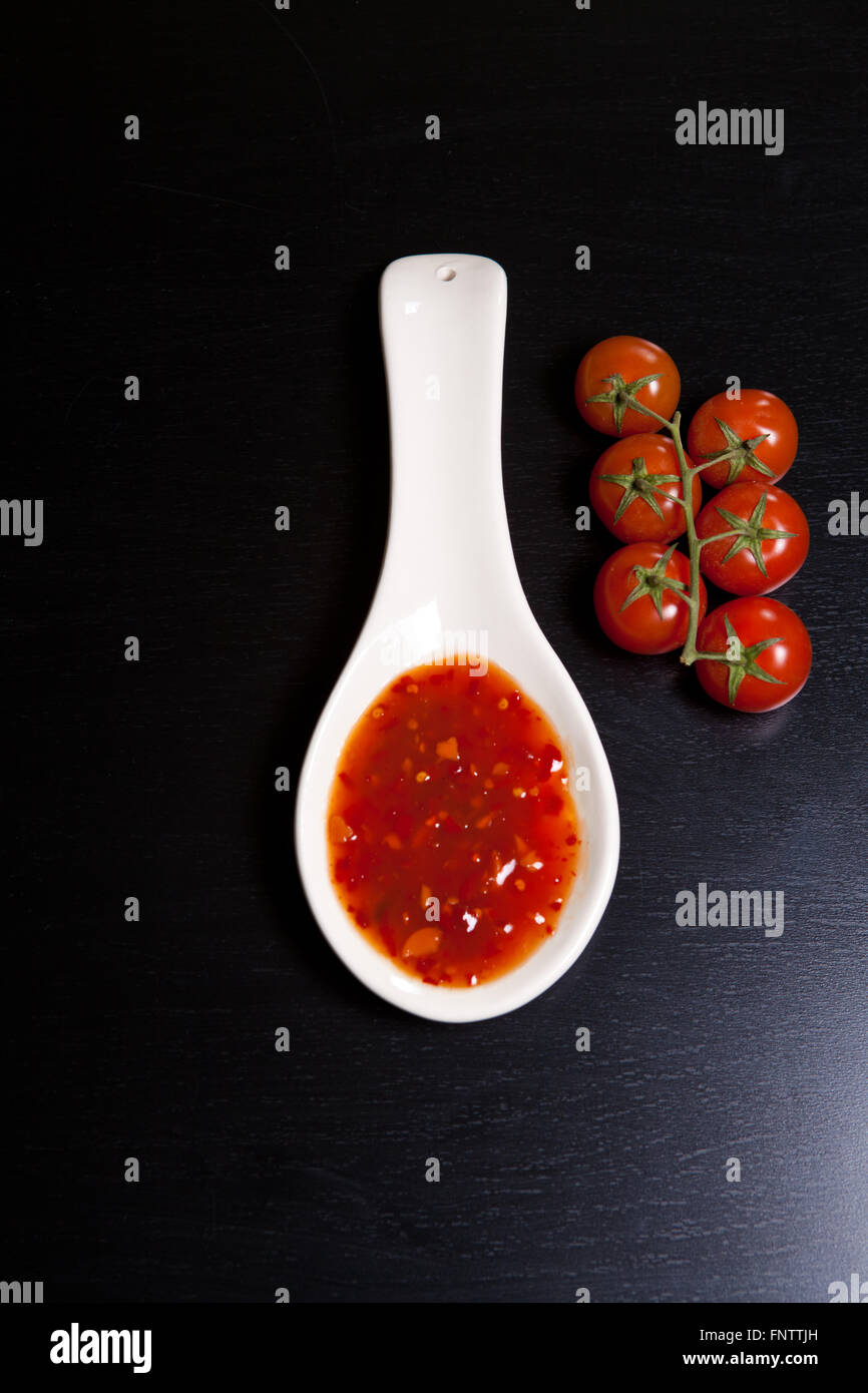 spicy tomato sauce in a gravy boat near cherry tomatoes on a dar Stock Photo