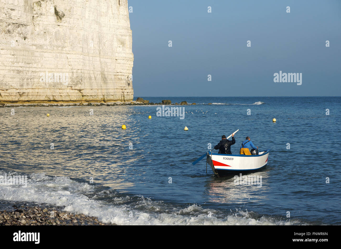 Two fishermen going out fishing in a small wooden boat at the coast of Normandy, France Stock Photo