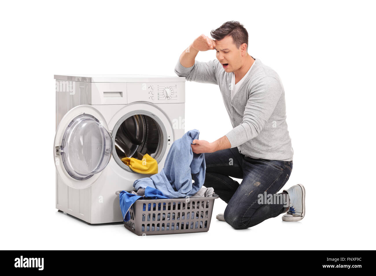 Studio shot of a displeased young man emptying a washing machine and looking at the clothes isolated on white background Stock Photo