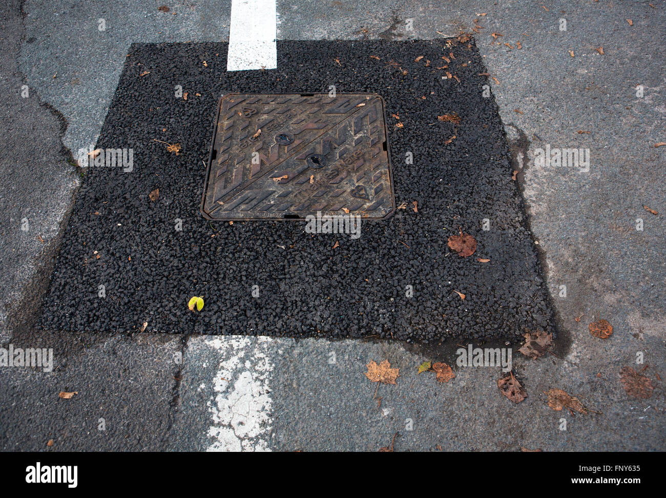 A fresh patch of new tarmac surrounding a man hole cover. Stock Photo