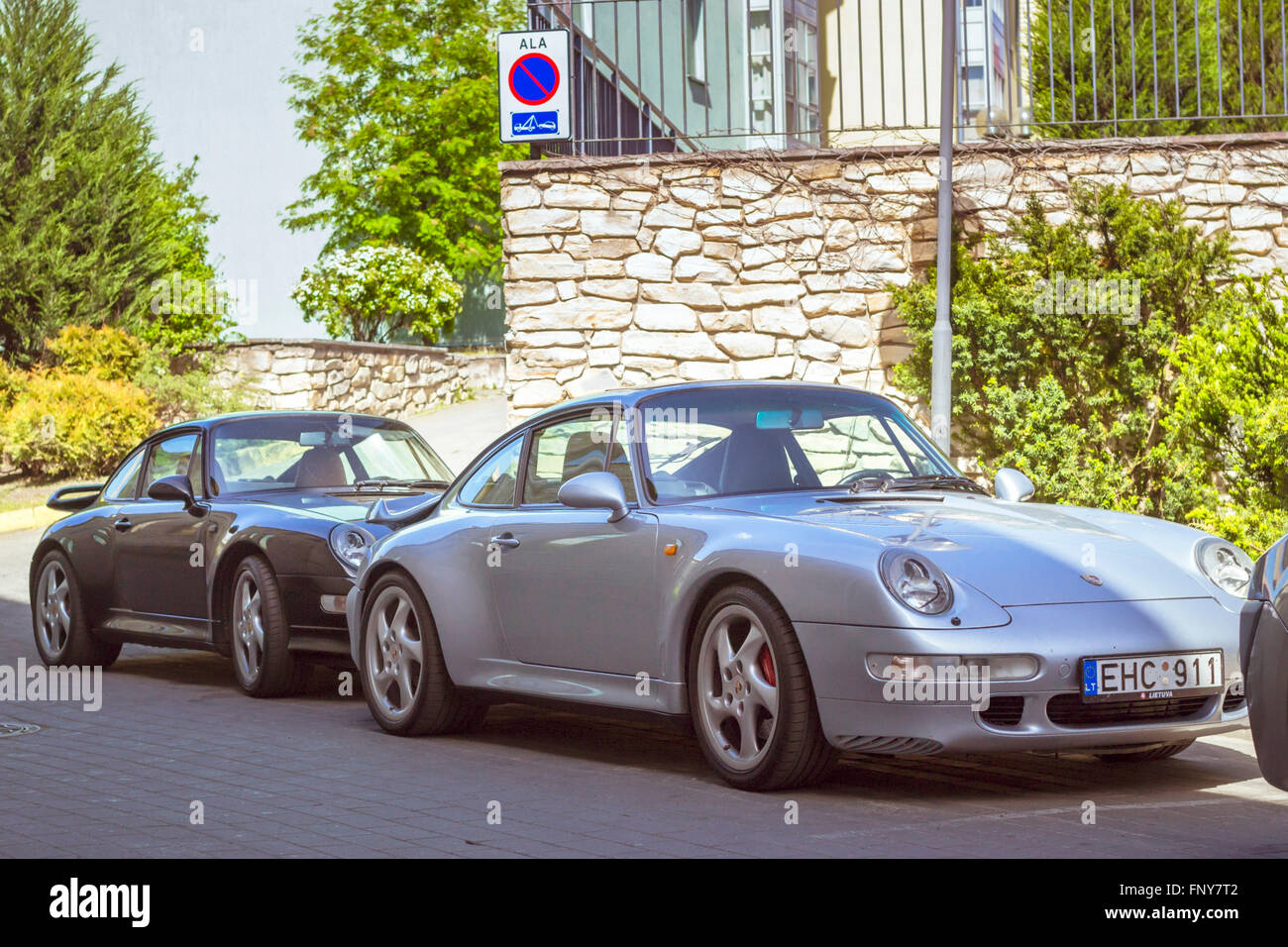 Tallinn, Estonia - June 12, 2015: Two sports coupe car Porsche parked in yard of the stone wall under the sign Parking Stock Photo