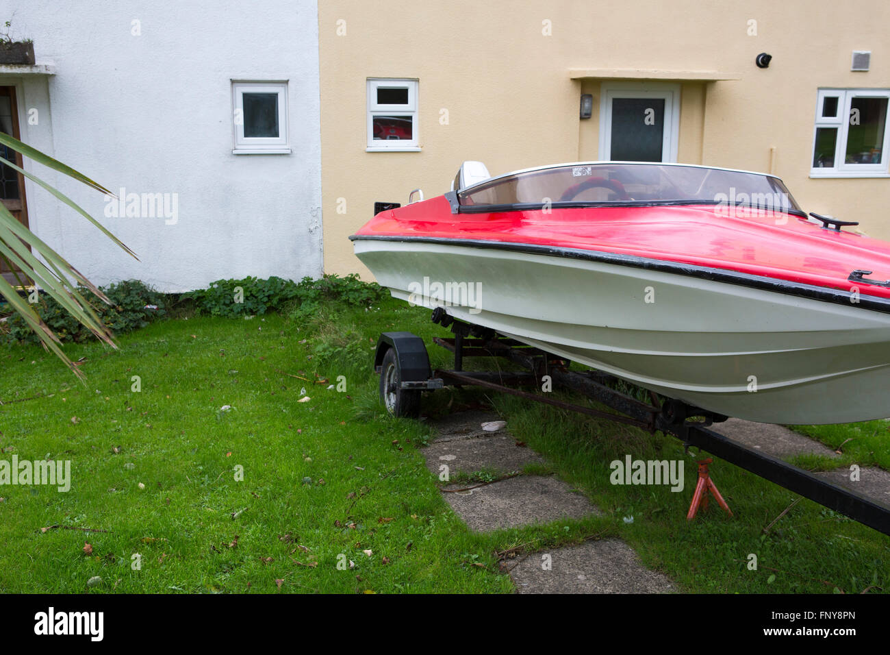 A red speed boat set at rest in the front garden of a UK home on an estate in Wlaes. Stock Photo