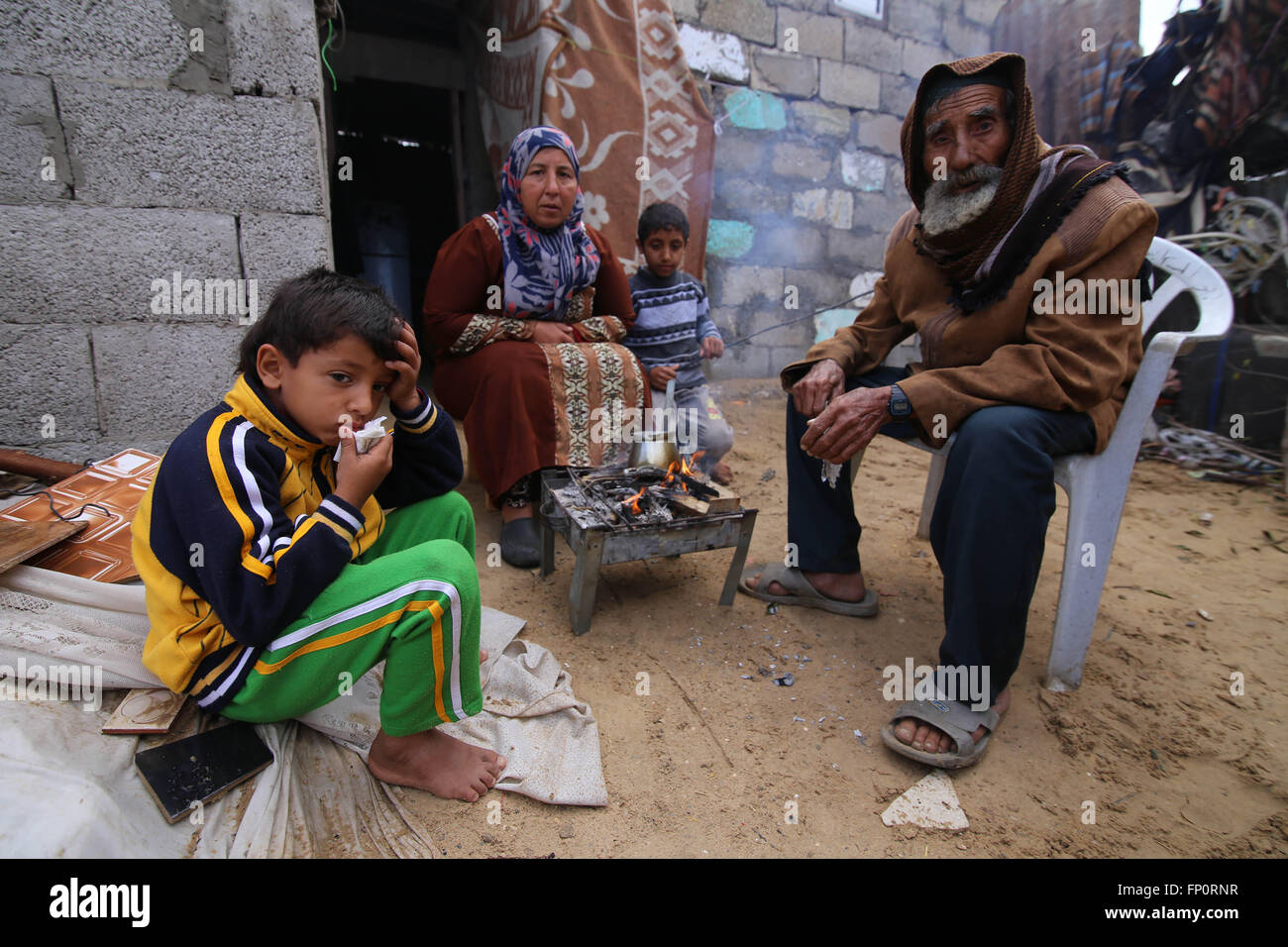 (160317) -- GAZA, March 17, 2016 (Xinhua) -- Palestinian Jihan Moussa Abu Mohsen, 48, sits with her family members near the fire inside their house in the southern Gaza Strip city of Khan Yunis, on March 17, 2016. Jihan, who works from the morning hours till late the day, sells a cart of bricks to stone manufacturers for 4 US dollars per day. Her work is the main source of income for her family which consists of her husband and four children. Jihan and her son Ahmad get up early every morning to collect bricks and stones from anywhere they find them, whether in landfills, streets or roadsides. Stock Photo