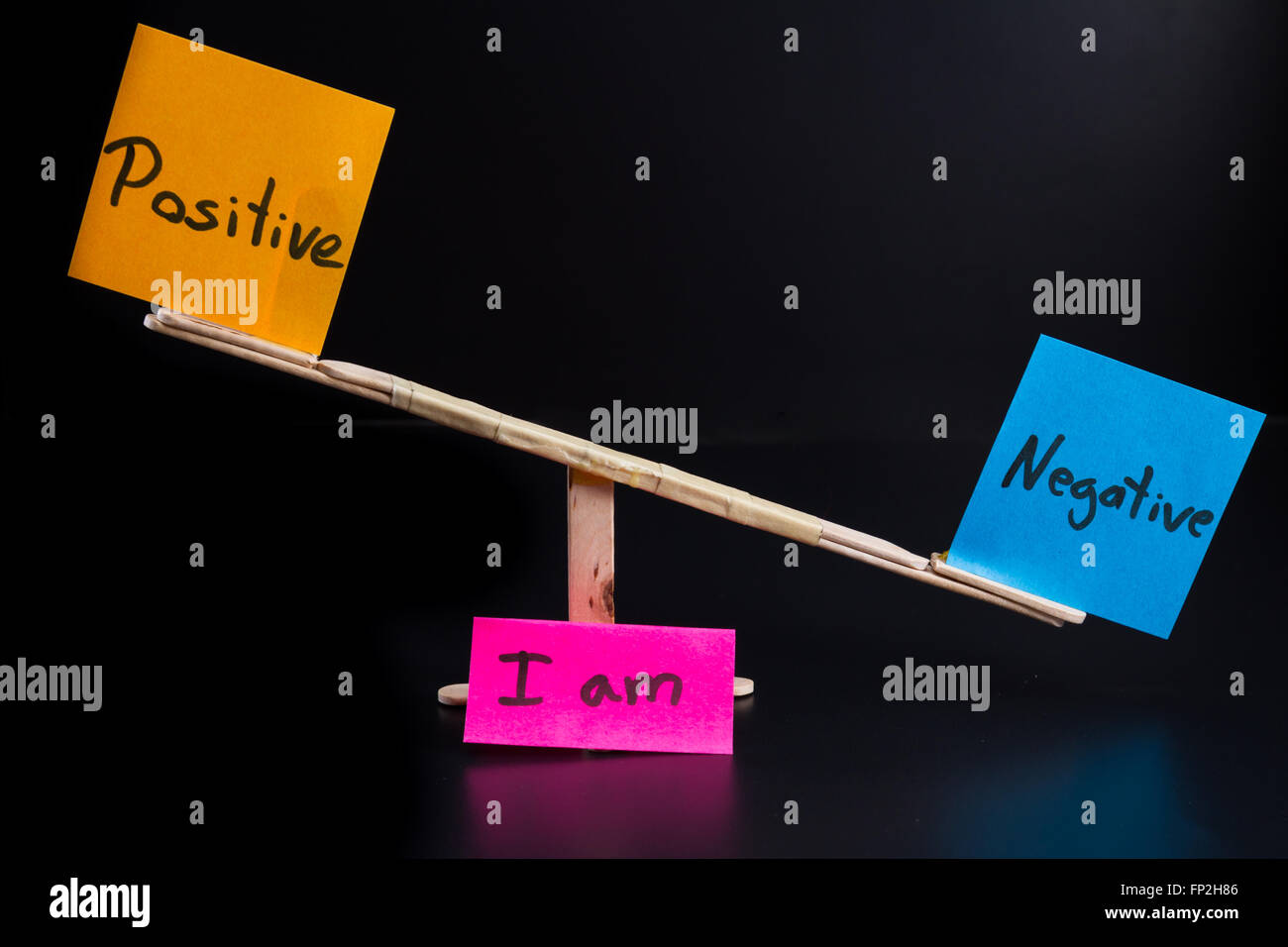 concept of duality using sticky notes with antonyms on a hand made sea saw on a dark background