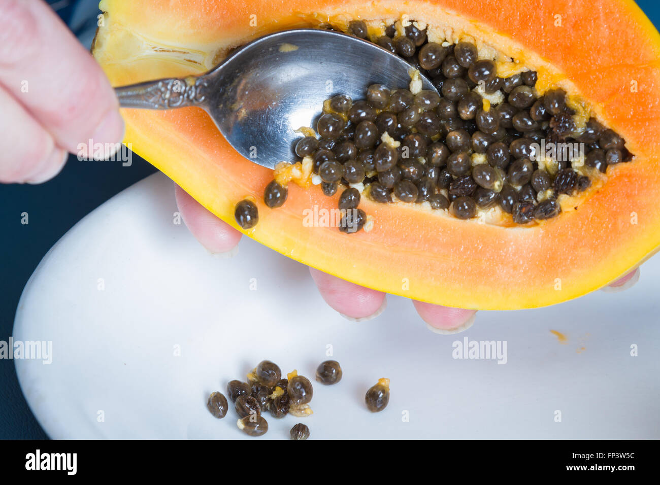 cleaning a papaya with a spoon up close dropping the seeds on a white