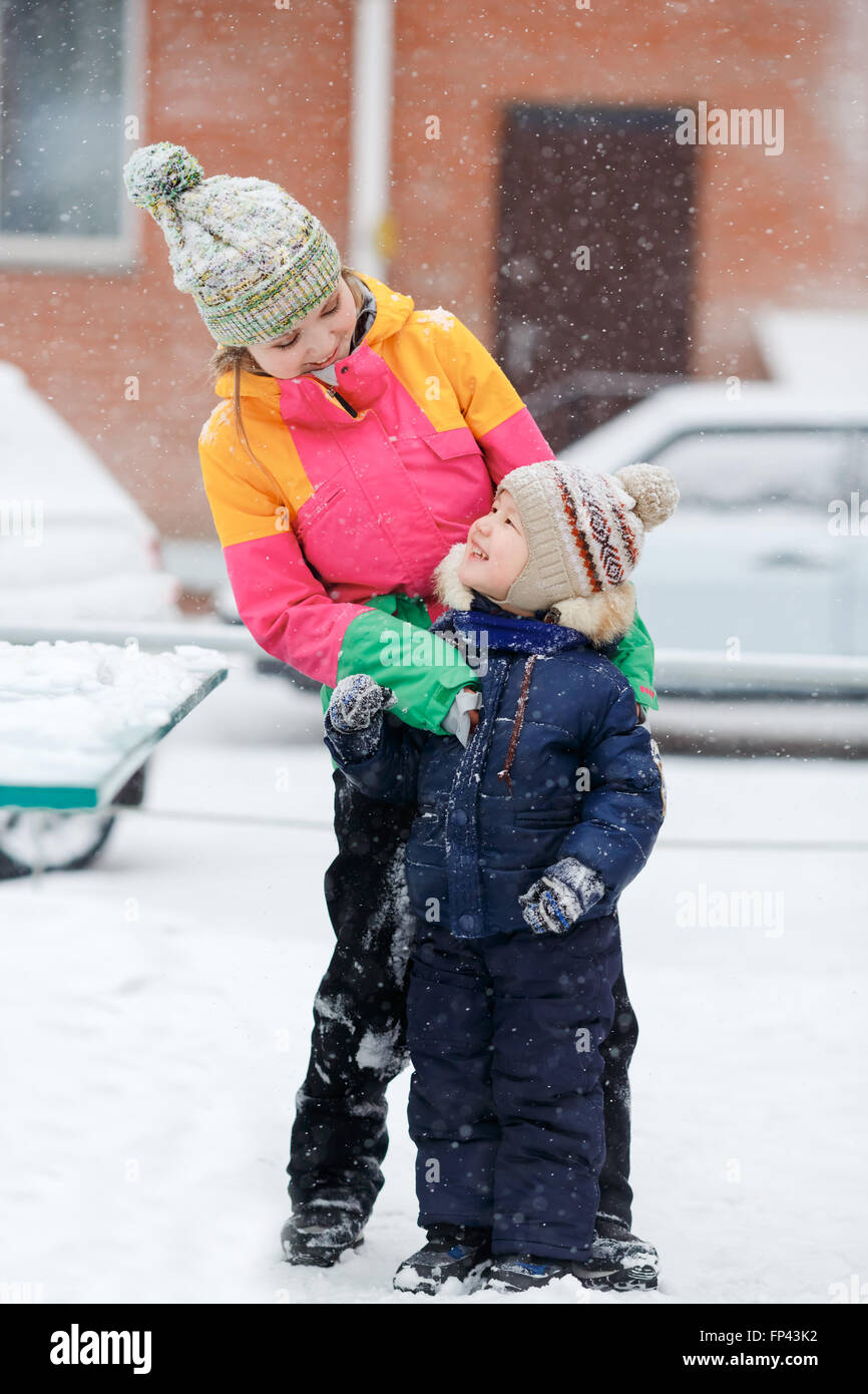 Mom with child playing outdoors at street in winter during snowfall. Stock Photo