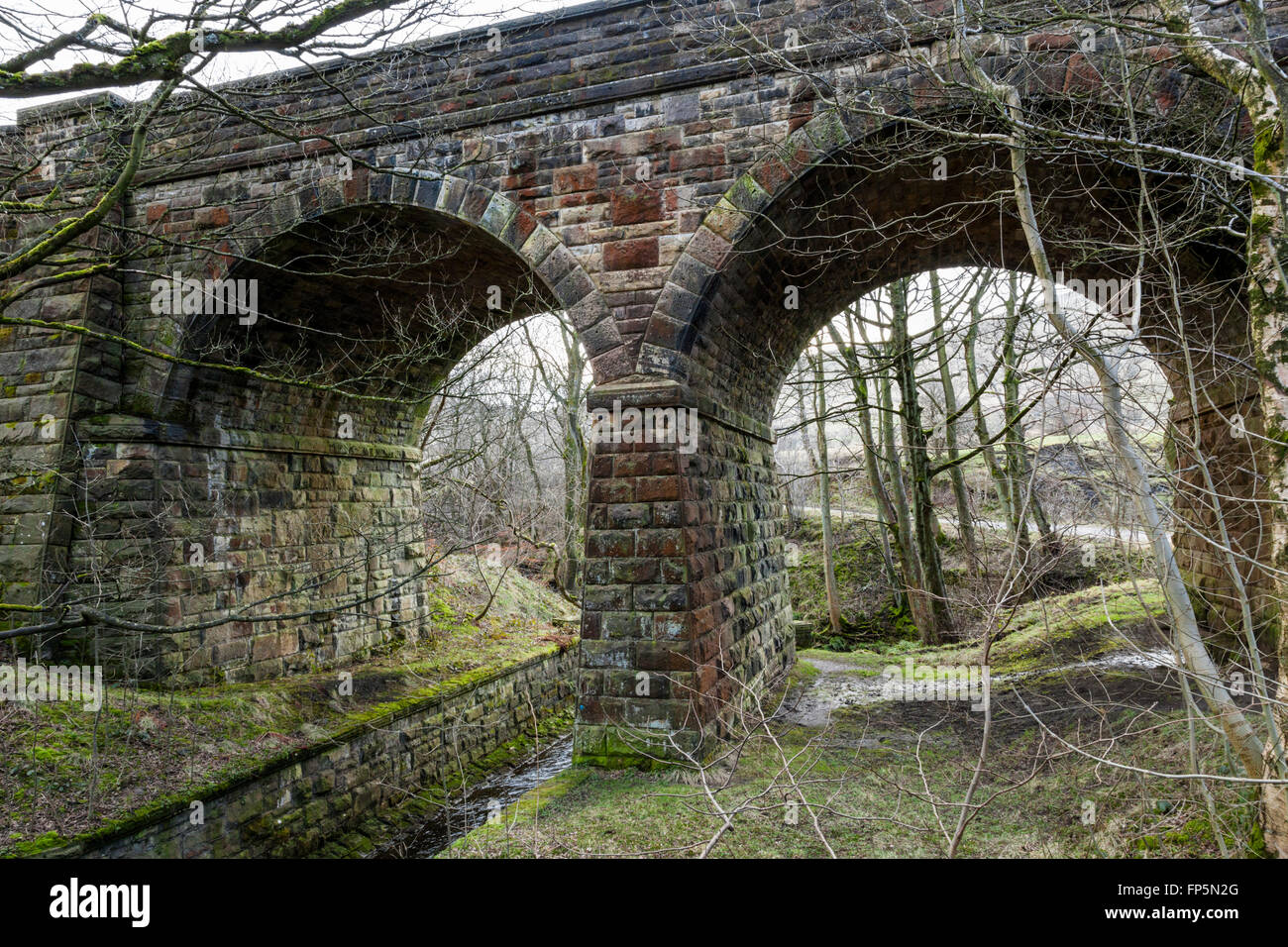 A stone railway bridge passing over a stream and next to trees, Barber Booth in Derbyshire, England, UK Stock Photo