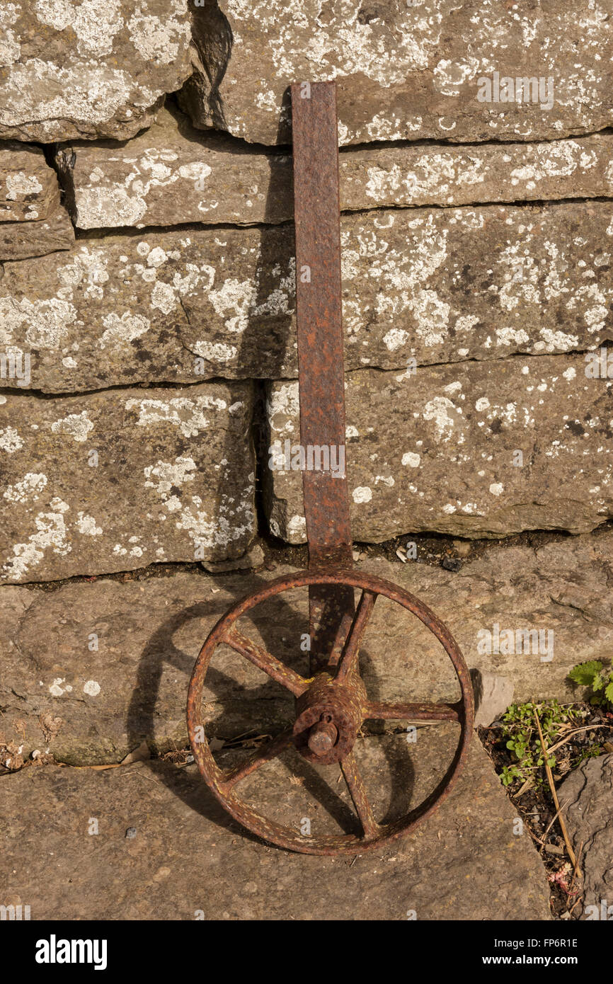 Rusty wheel leaning against a stone wall Stock Photo