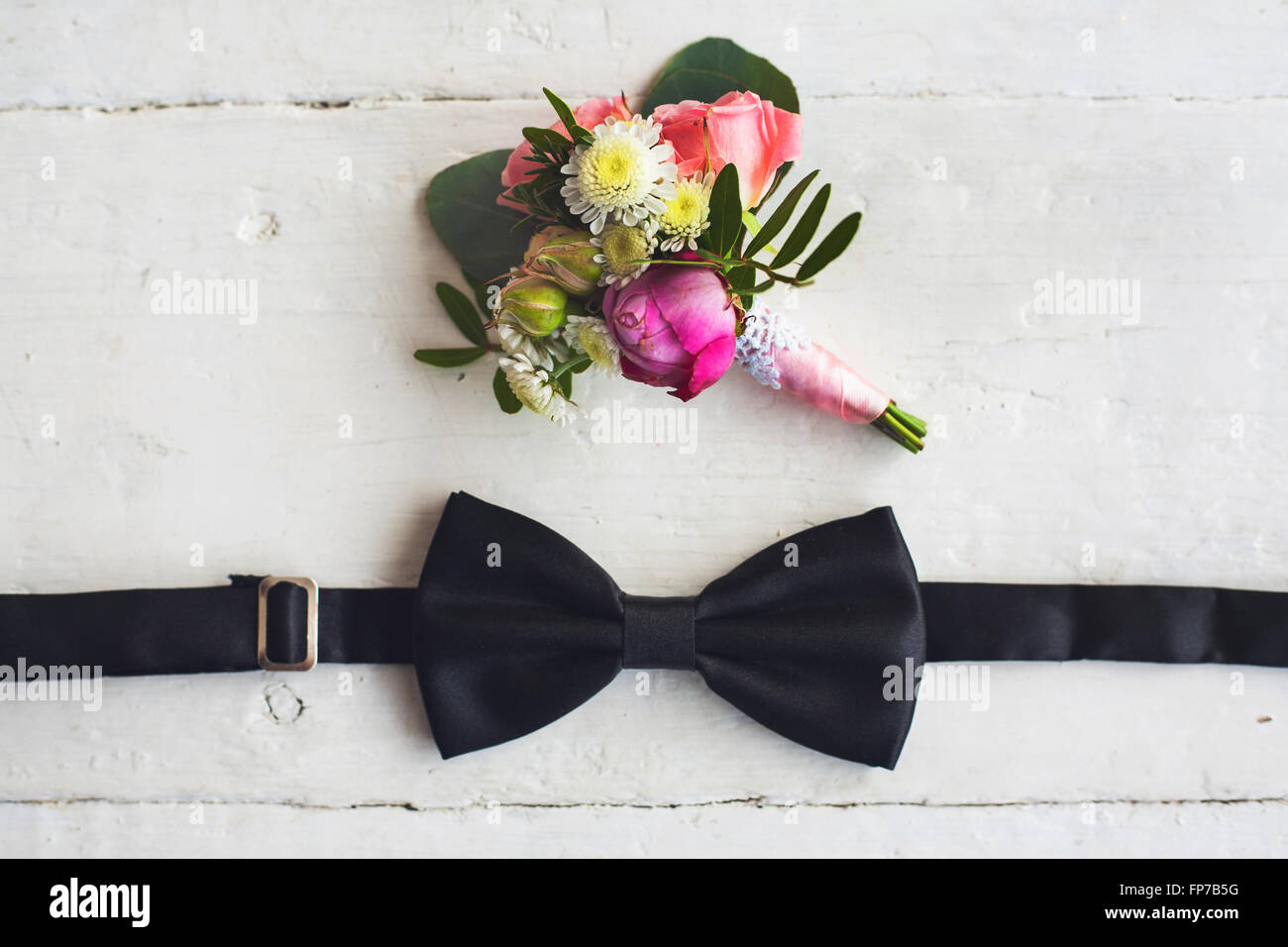 Close up of man accessories. Black bowtie and flower boutonniere on white wood rustic background. Set for formal style of wearin Stock Photo