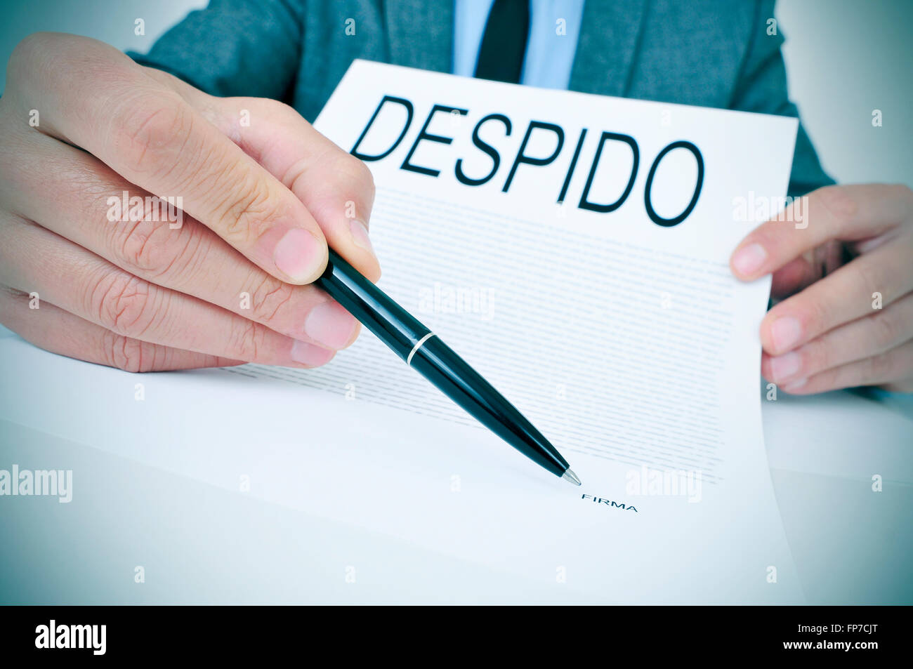a young caucasian businessman sitting at his office desk shows a document with the word despido, dismissal written in spanish, a Stock Photo