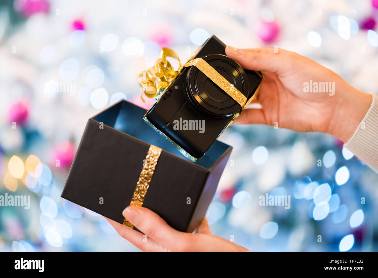 Woman discovers a digital compact photo camera in Christmas present. Boke christmas tree background Stock Photo