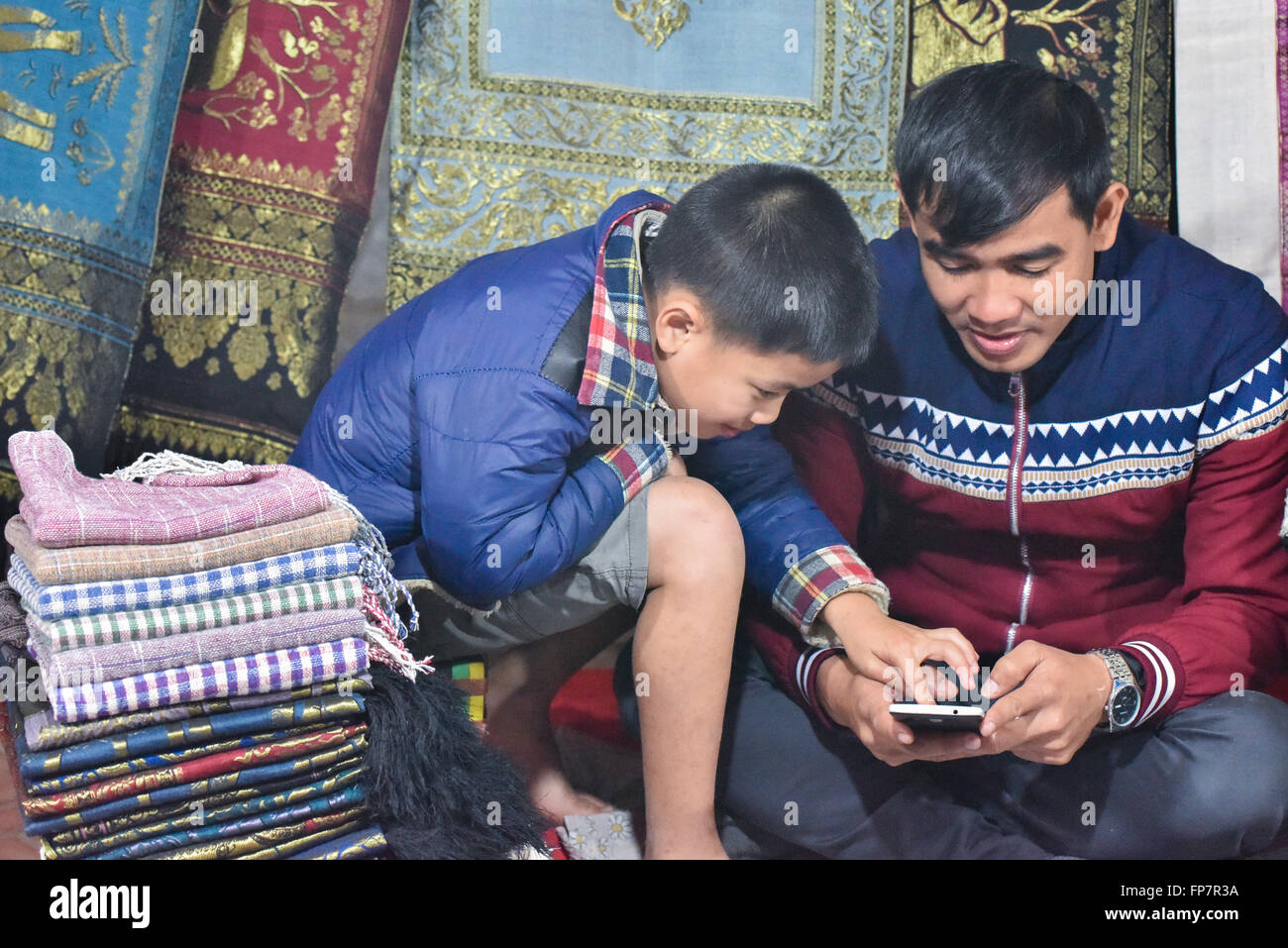 Salesman and his son looking at mobile phone Luang Prabang Night market Laos Stock Photo