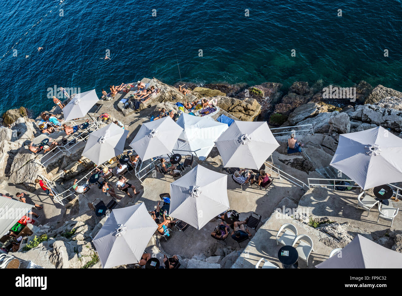 restaurant umbrellas on the rocks under the Old Town Walls of Dubrovnik in Croatia Stock Photo