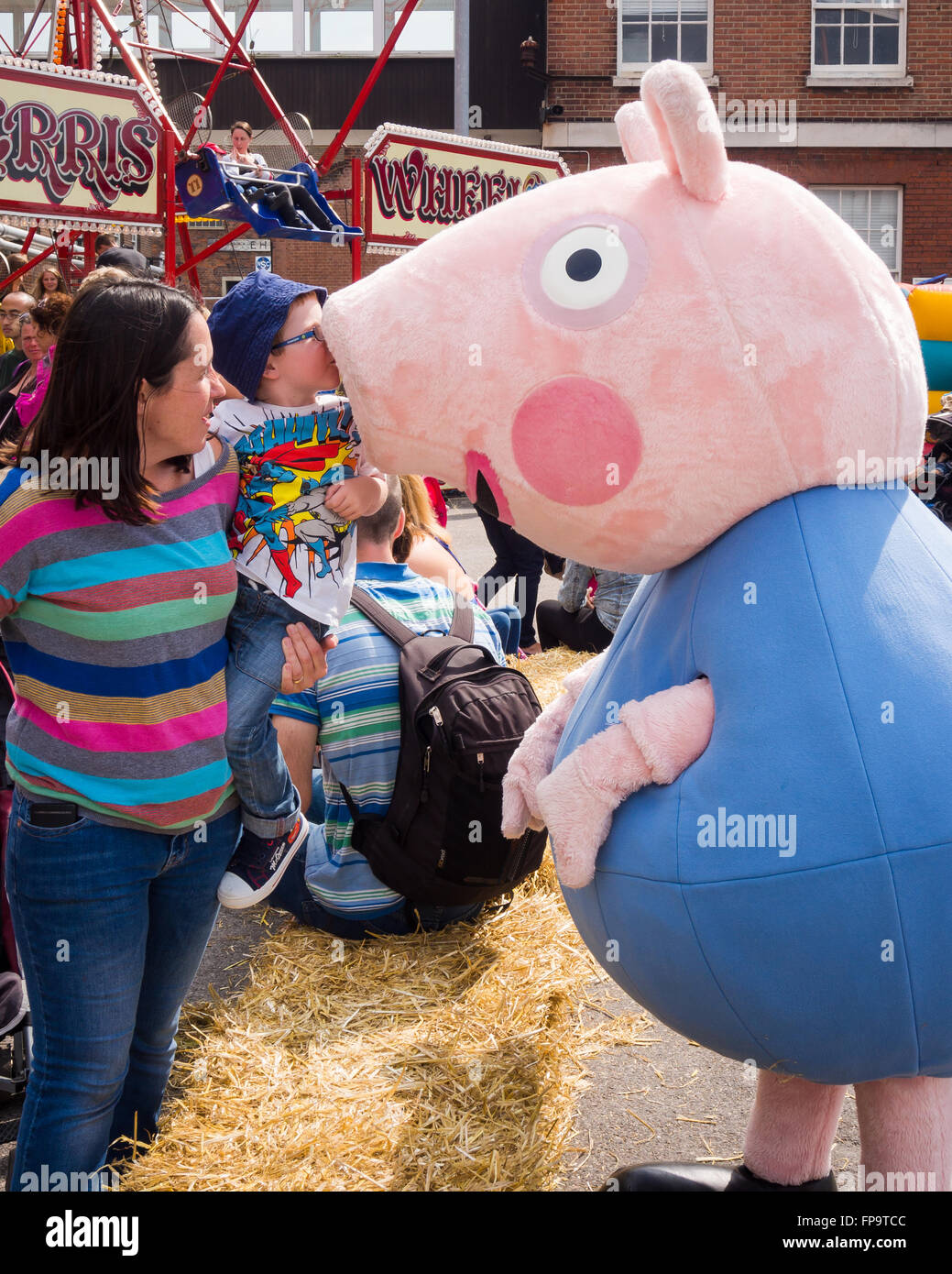 A mother holds a young boy up so that he can give George pig a kiss Stock Photo