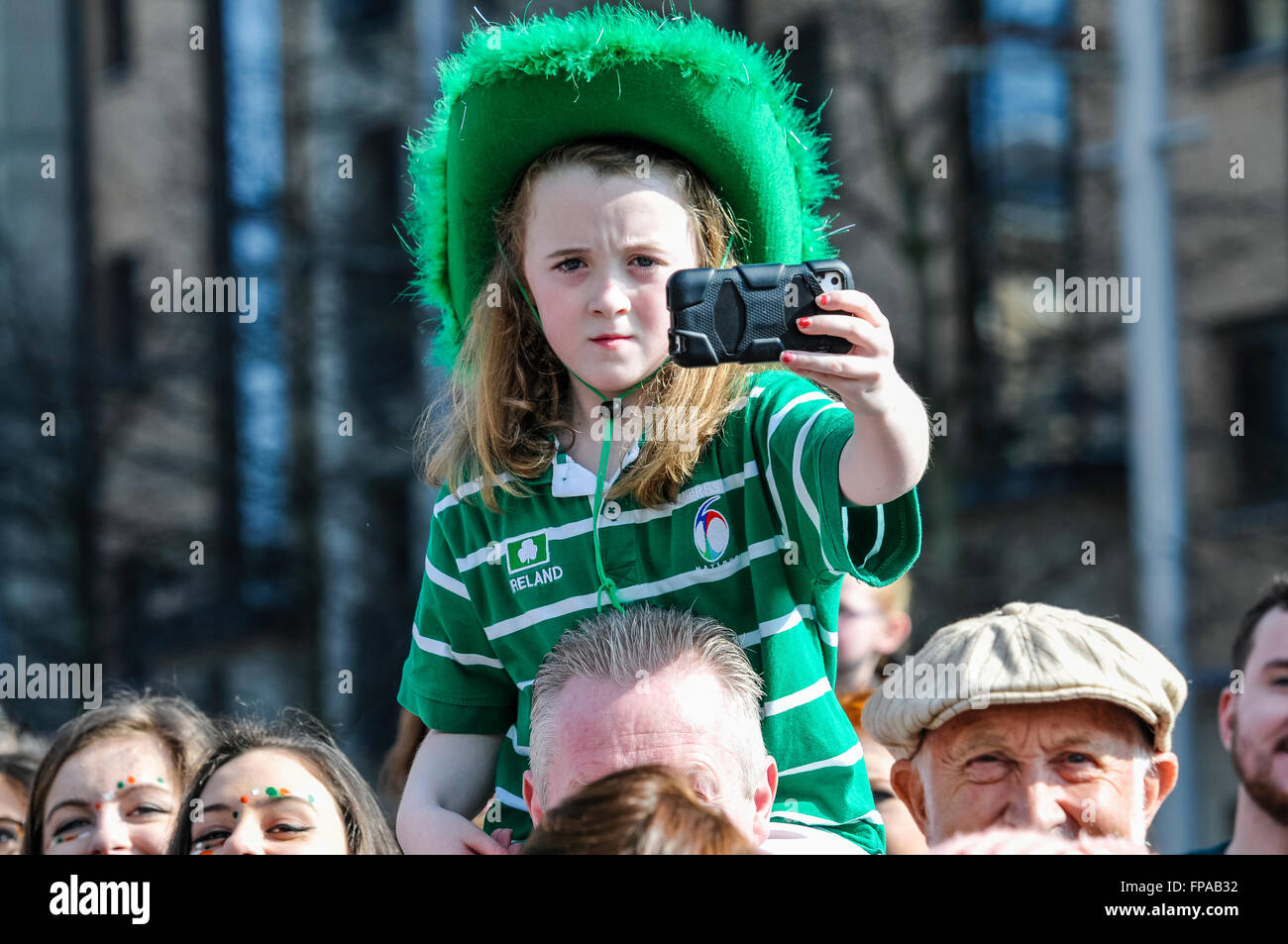 Belfast, Northern Ireland, UK. 17th March, 2016. A young girl on her daddy's shoulders uses a smartphone to record the annual Saint Patrick's Parade. Credit:  Stephen Barnes/Alamy Live News Stock Photo