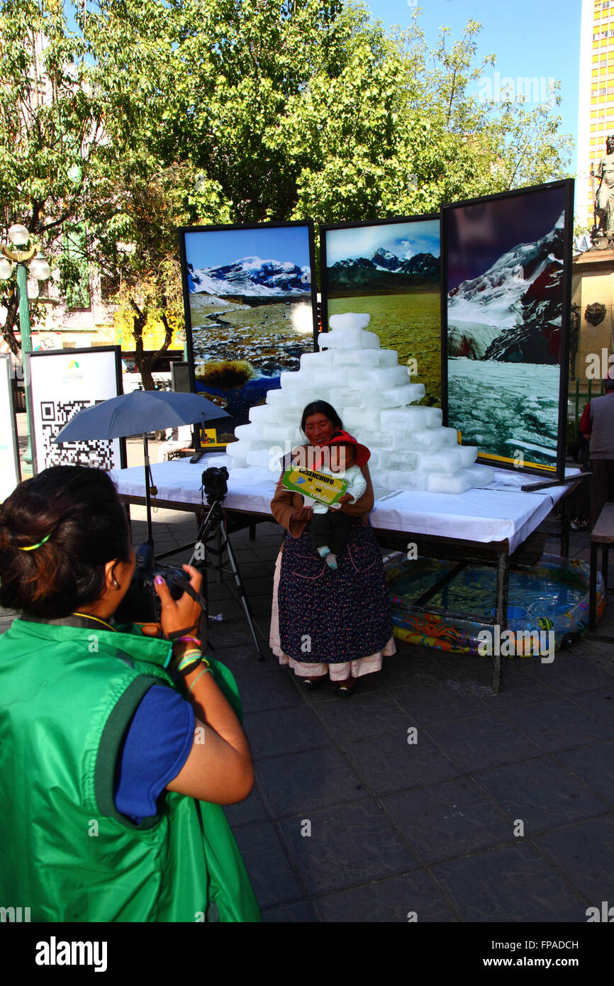 La Paz, Bolivia, 18th March 2016. A municipal worker takes photos of members of the public holding placards with ways to help protect the environment in front of melting ice blocks and photos of Bolivia's mountains. The event was organised by the La Paz City Government to highlight global warming for Earth Hour (which takes place tomorrow). The glaciers in Bolivia and the Andes are some of the fastest receding on the planet, causing environmental changes and water shortages in many parts of the region. Credit:  James Brunker / Alamy Live News Stock Photo
