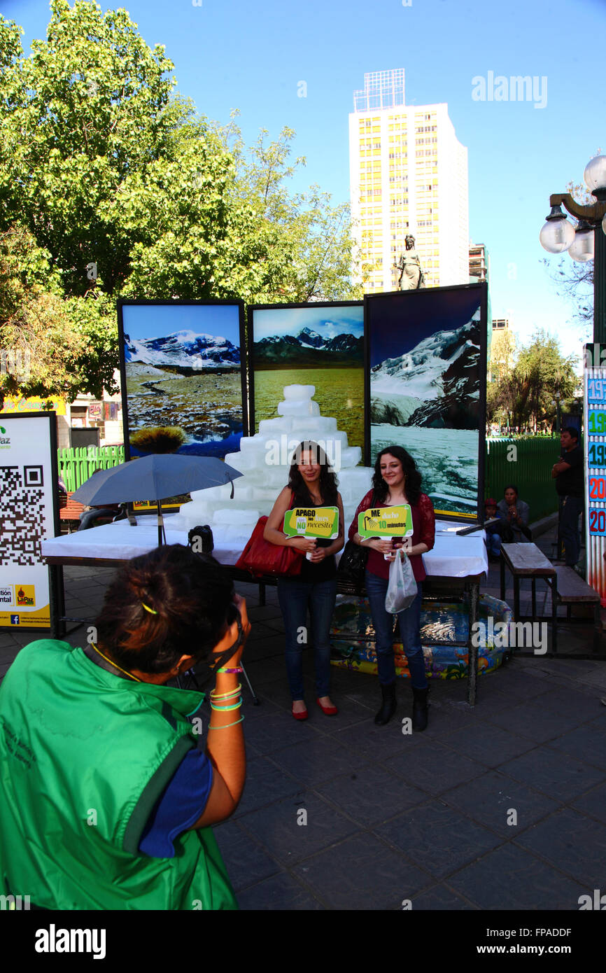 La Paz, Bolivia, 18th March 2016. A municipal worker takes photos of members of the public holding placards with ways to help protect the environment in front of melting ice blocks and photos of Bolivia's mountains. The event was organised by the La Paz City Government to highlight global warming for Earth Hour (which takes place tomorrow). The glaciers in Bolivia and the Andes are some of the fastest receding on the planet, causing environmental changes and water shortages in many parts of the region. Credit:  James Brunker / Alamy Live News Stock Photo
