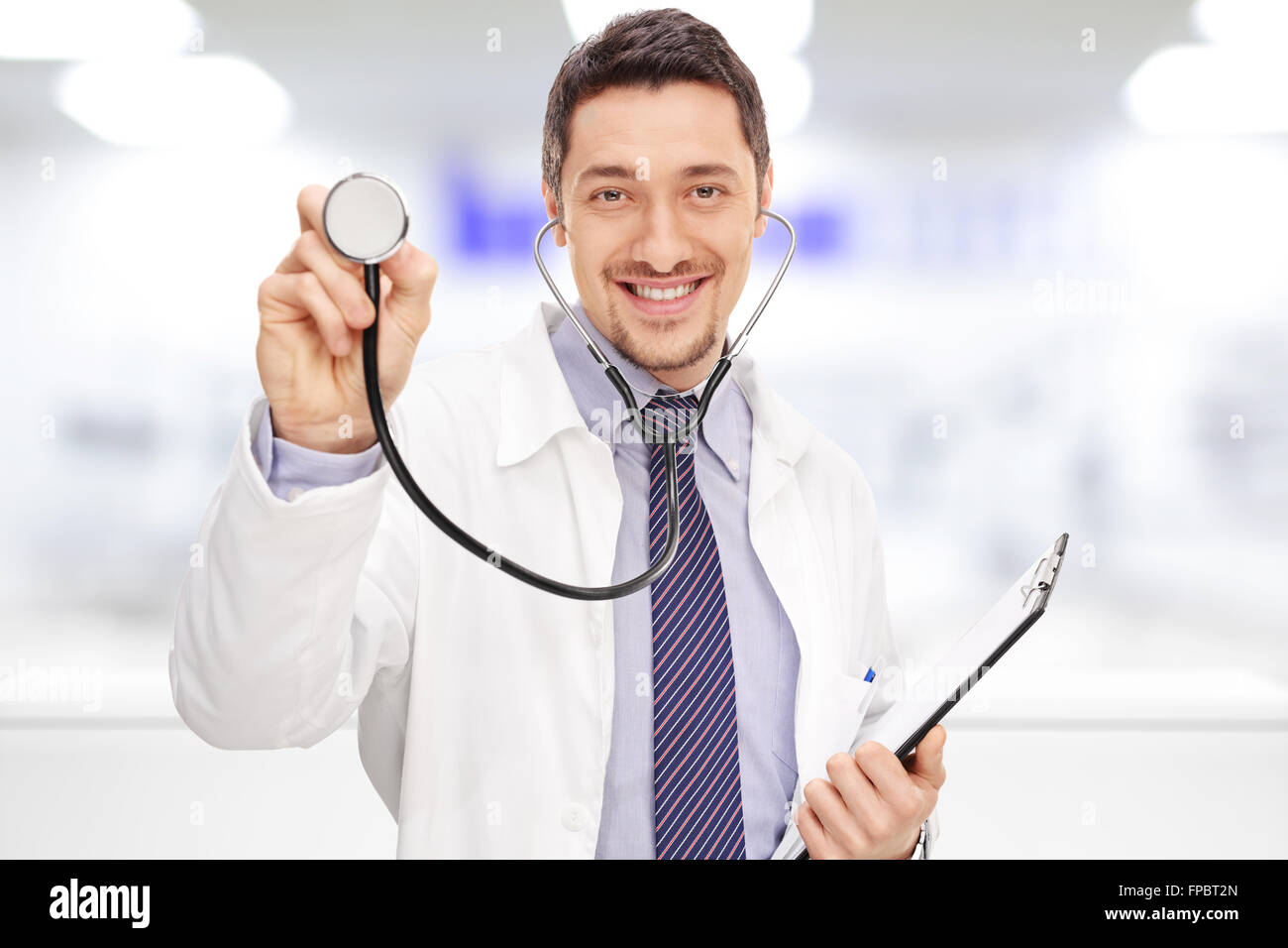 Young cheerful doctor holding a stethoscope and a clipboard in a hospital Stock Photo