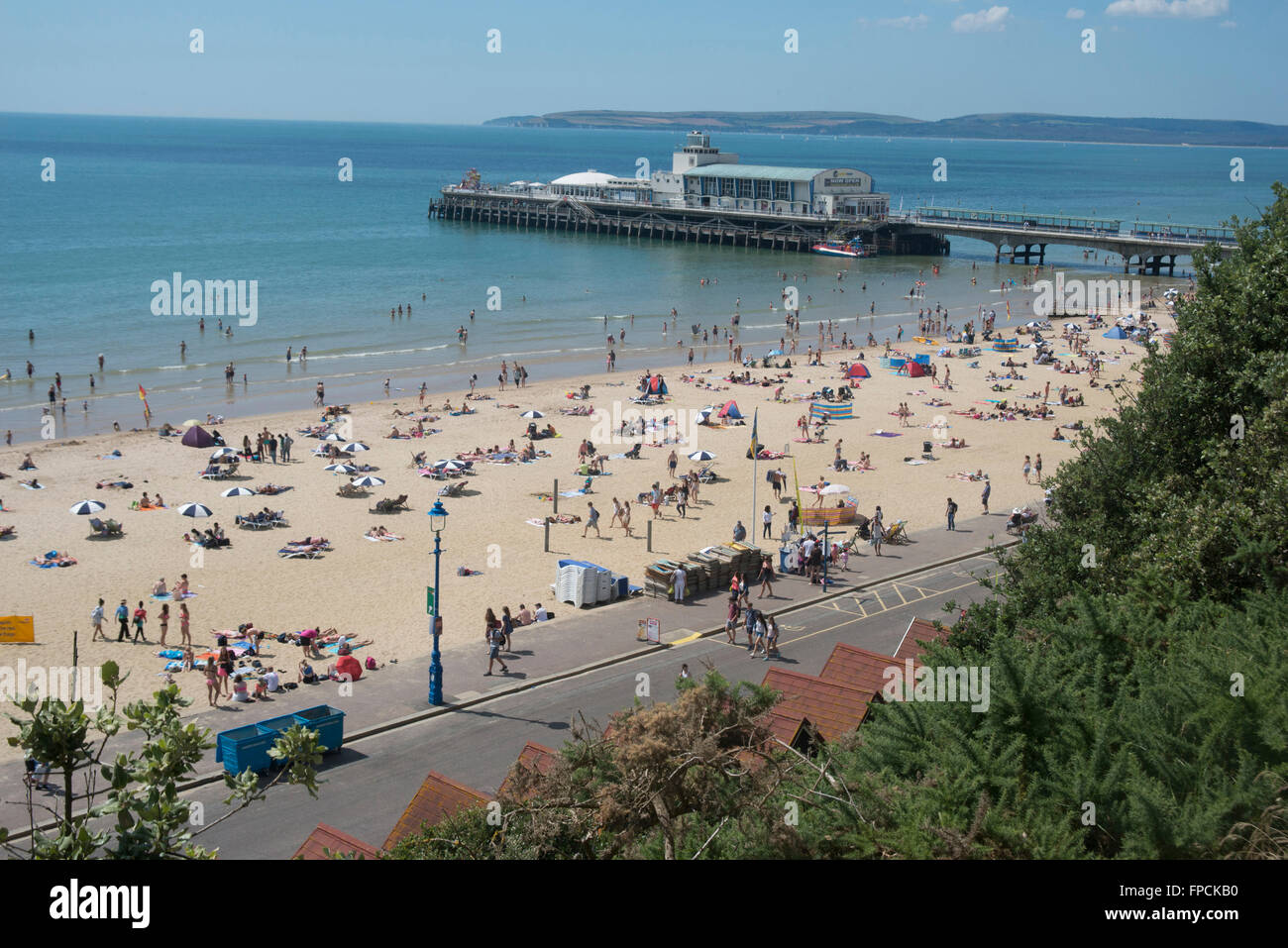 A view from above of the beach filled with people, the pier can be seen in the distance. Stock Photo