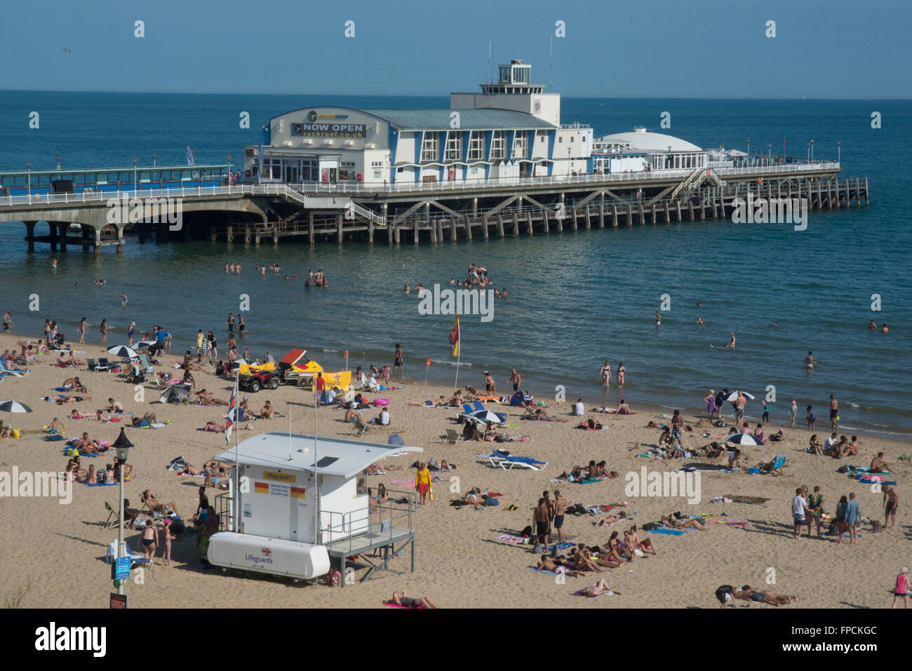 A view from above of the beach filled with people, the pier can be seen in the distance. Stock Photo