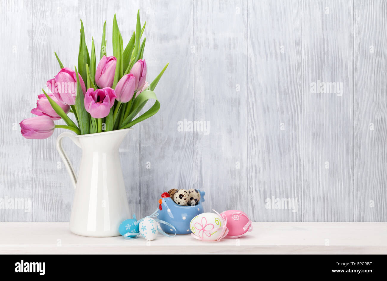 Easter eggs and pink tulips bouquet on shelf in front of wooden wall ...