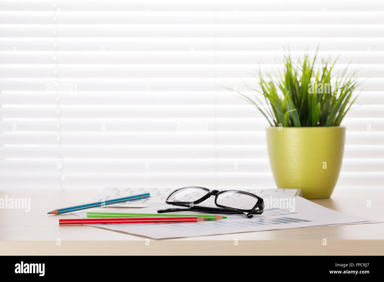 Office workplace with supplies and plant on wood desk table in front of window with blinds Stock Photo