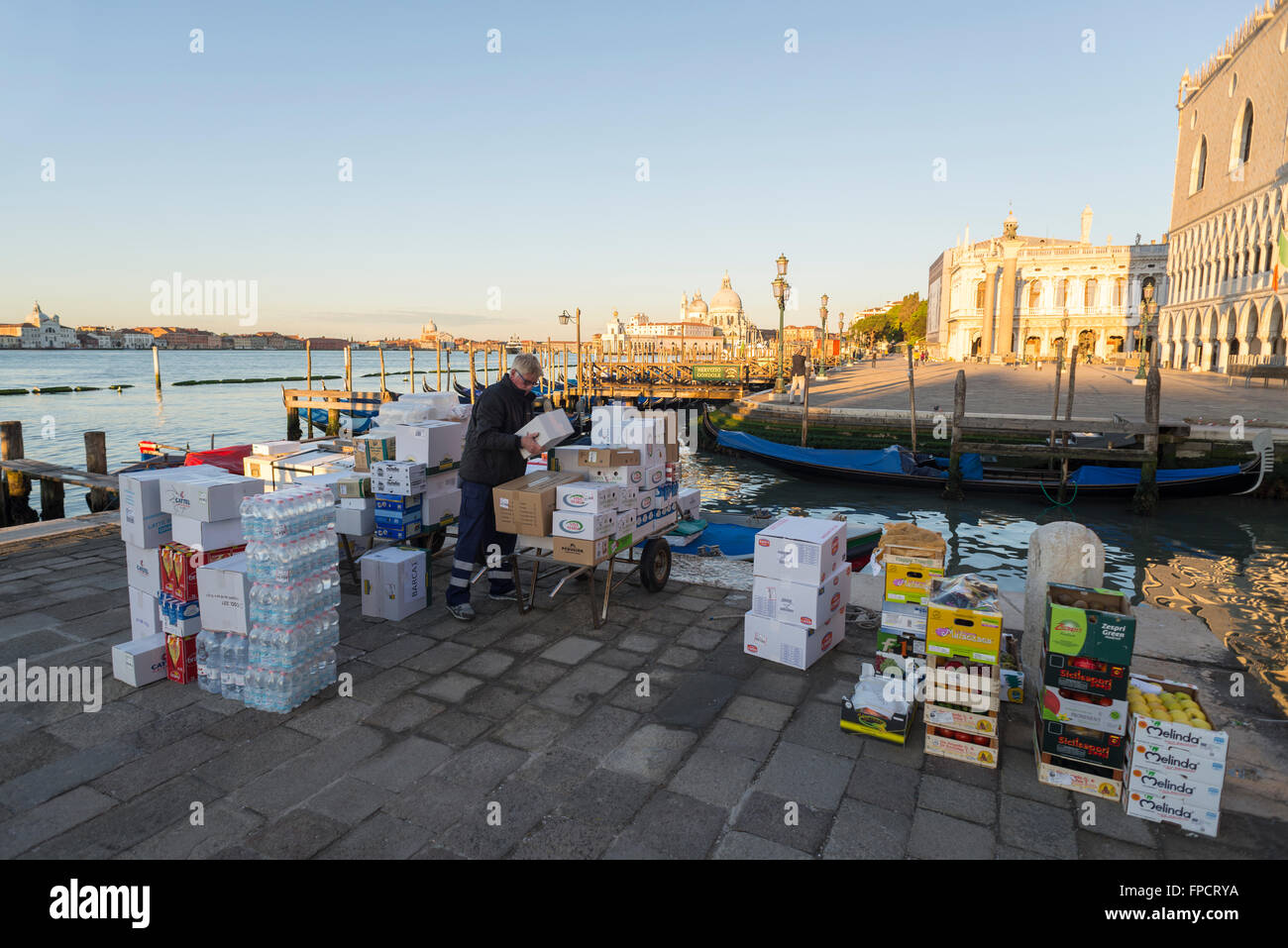 Male porter loads his hand truck with boxes from his barge on the quay of the little St. Mark's Square in Venice at sunrise Stock Photo