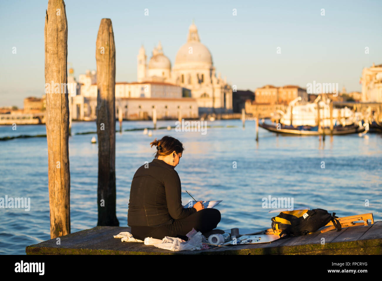 Woman sitting on a jetty near the St. Mark's Square at sunrise painting the cityscape of Venice at the Grand Canal Stock Photo
