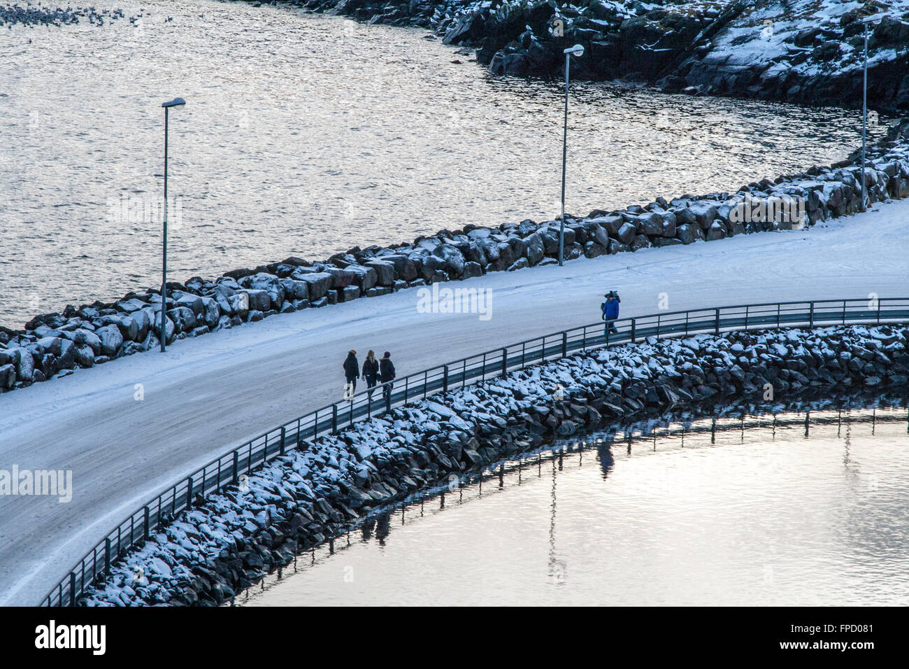 Three girls and a man with a rucksack walking towards eachother on an icy bridge in Stykkisholmur, Iceland Stock Photo