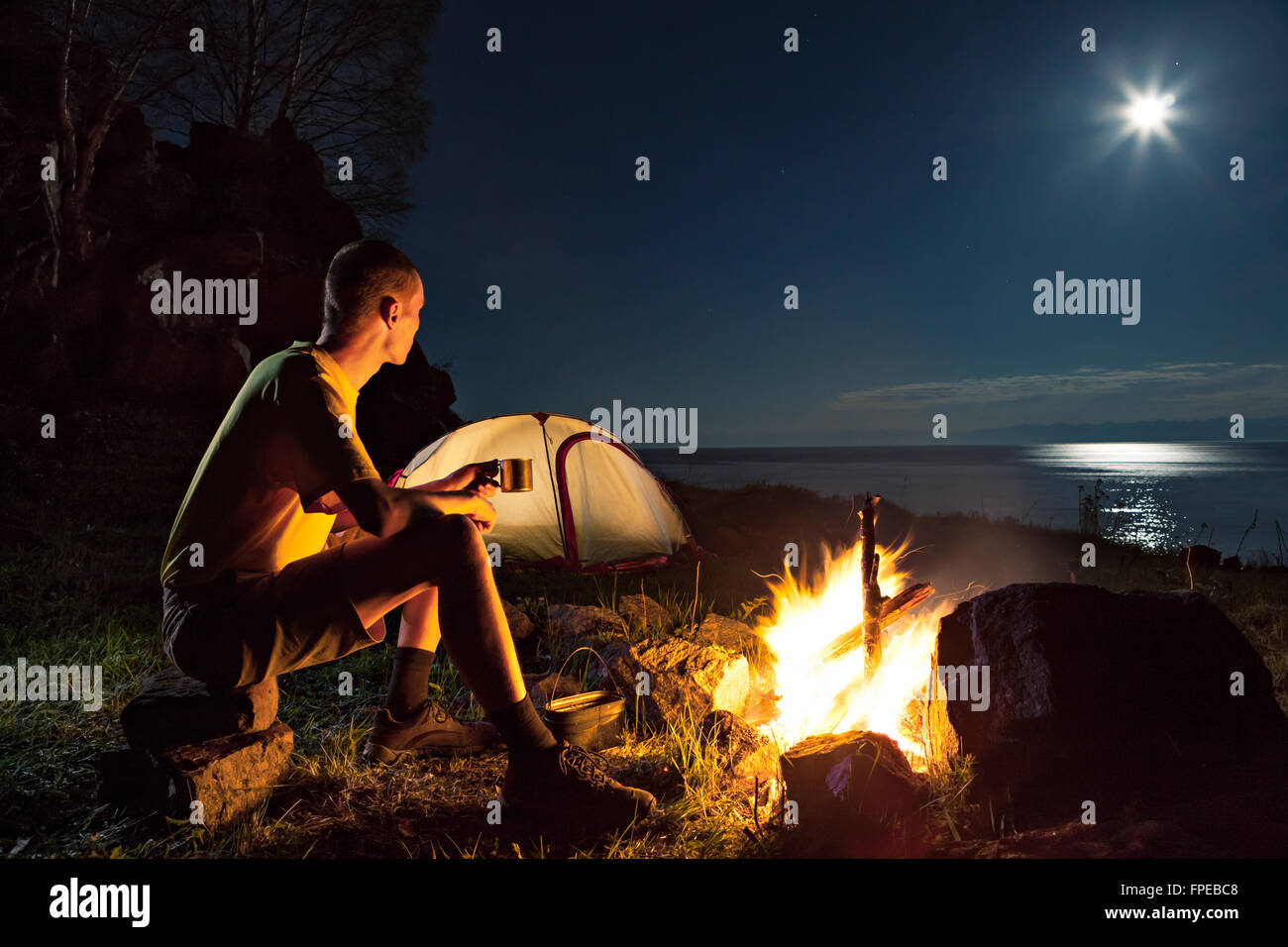 Hiking tourist have a rest in his camp at night near campfire Stock ...