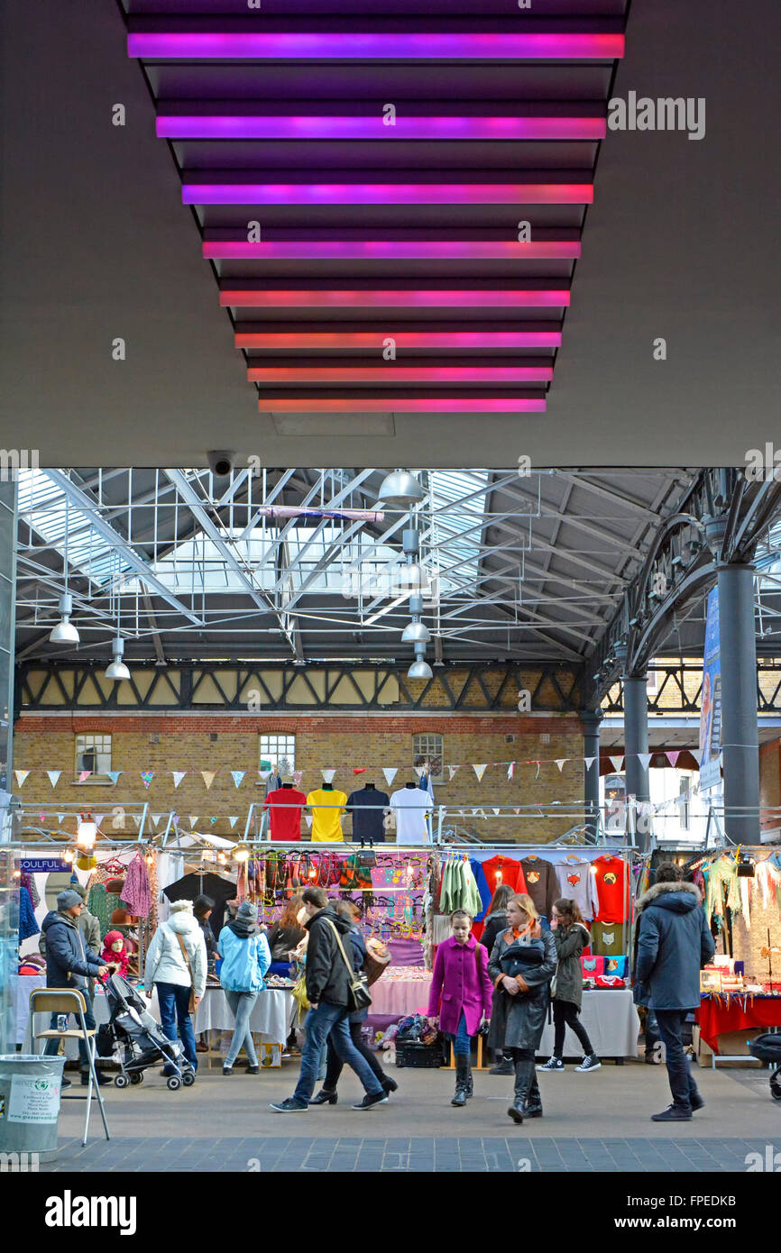 People attending Spitalfields old covered market variable coloured lighting panels above wide access corridor Tower Hamlets, London England UK Stock Photo