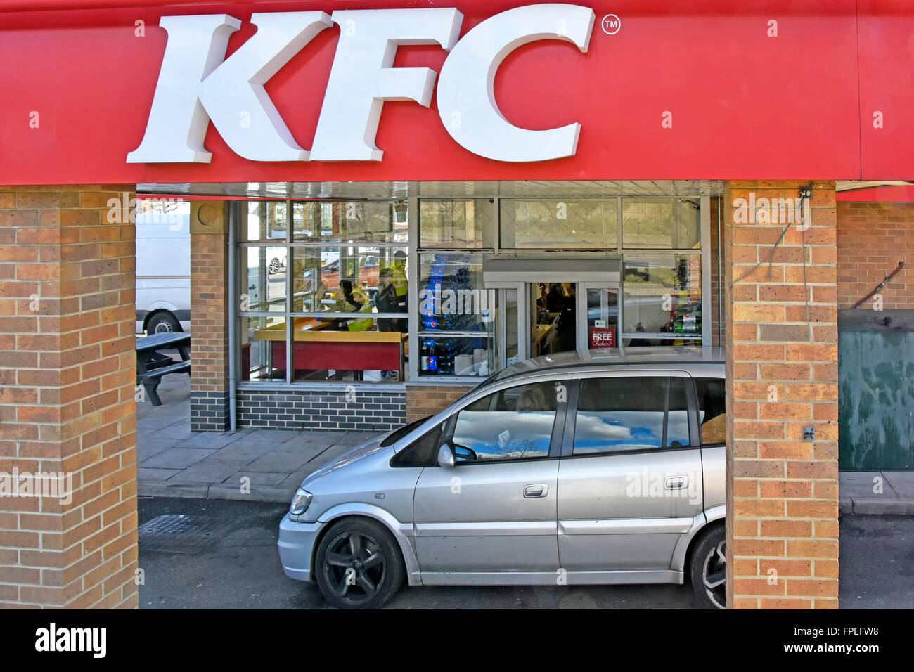 Kentucky Fried Chicken fast food restaurant drive through option &  customer sitting in car at ordering payment window below large KFC logo sign UK Stock Photo