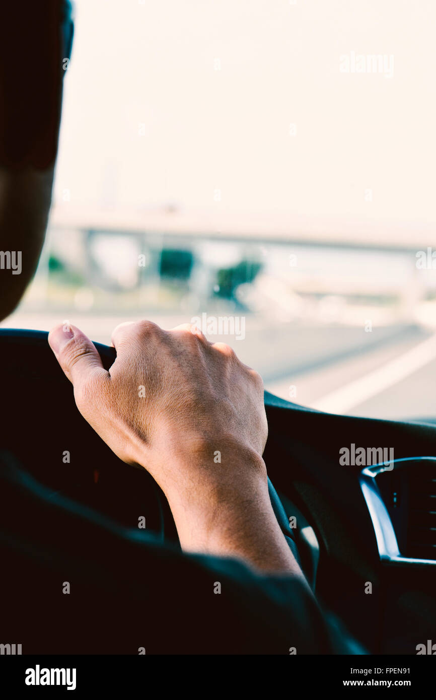 closeup of a young caucasian man, seen from behind, driving a car in a road with several lanes Stock Photo
