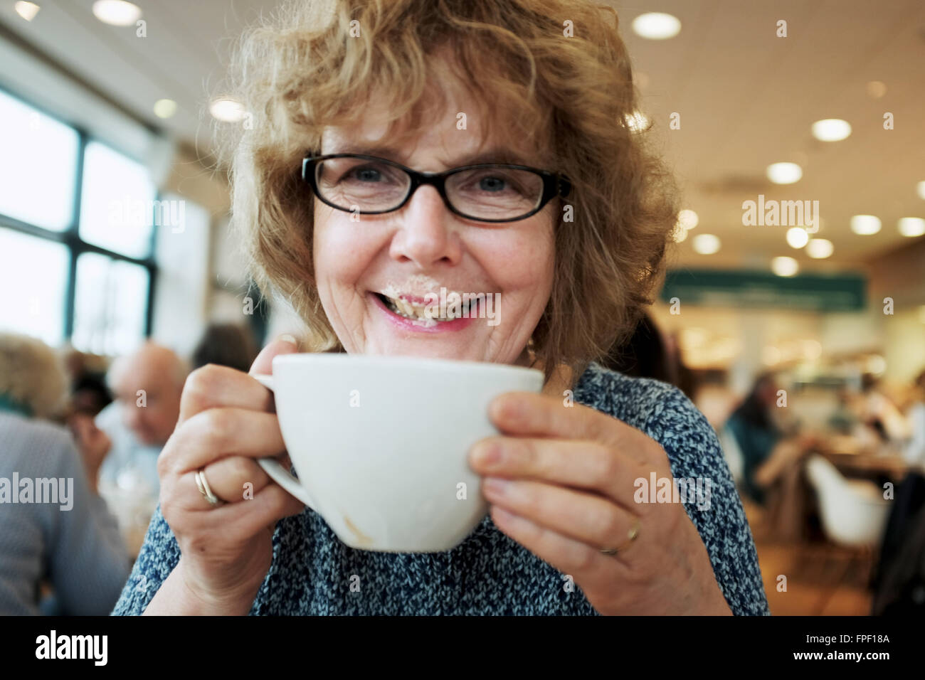 Middle aged woman enjoying a cup of cappuccino coffee in a cafe getting the cream on her lips and nose Stock Photo