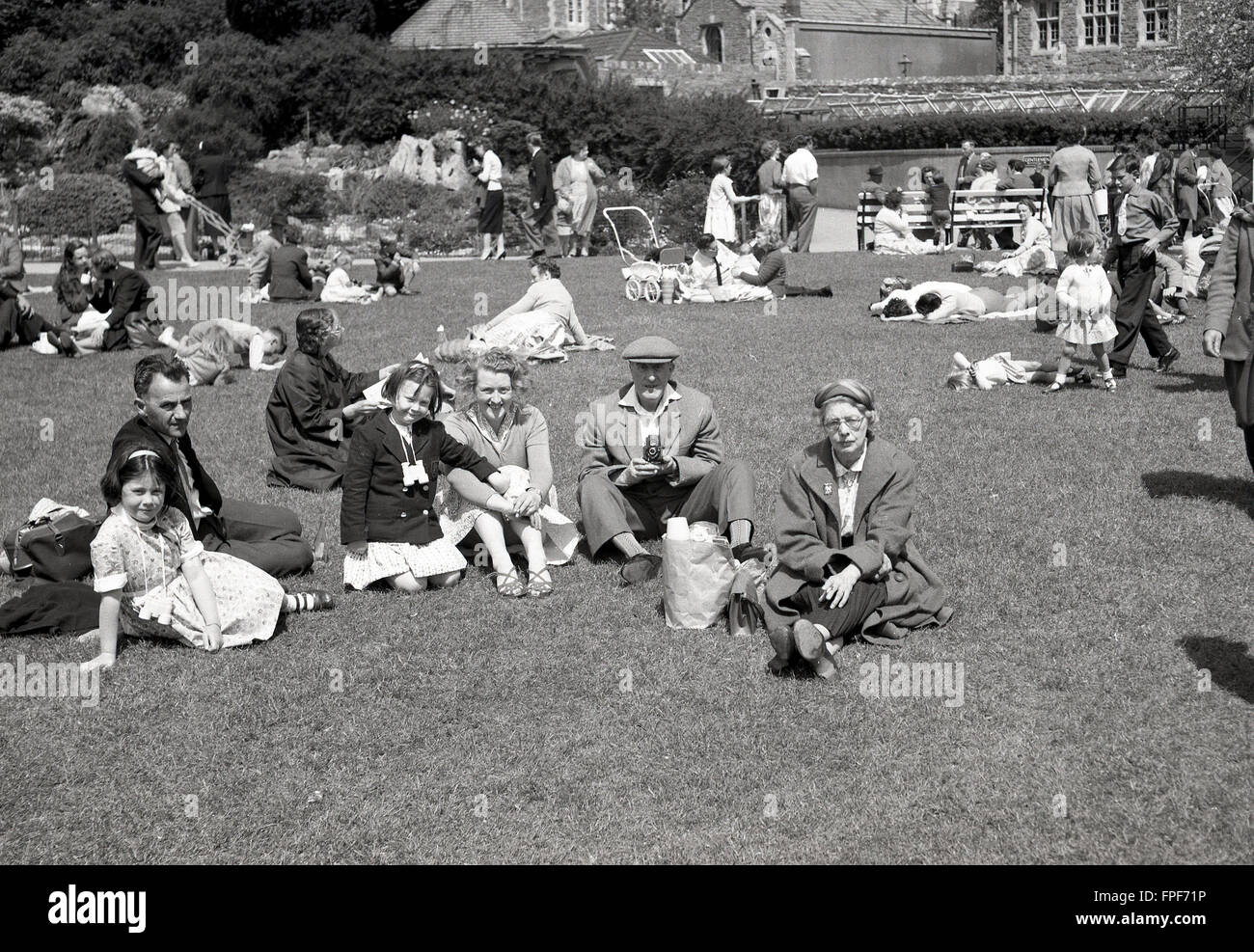 1950s historical, family sitting on grass outside historic house. Stock Photo