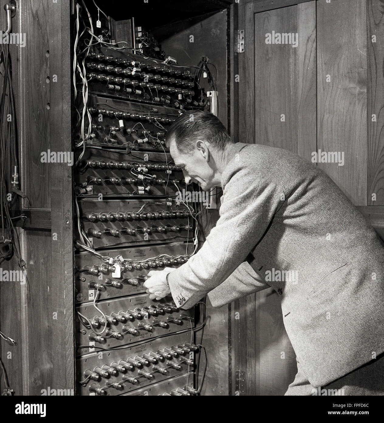 1950s historical, a man moving dials on a control panel or circuit board at the transatlantic cable station in Waterville, Co. Kerry, Ireland. once home to the one of the largest cable stations in the world. The first successful transatlantic telegraph message was transmitted through there in 1884, after the Commerical Cable Co had laid two cables across the Atlantic ocean connecting Canada, Britain and France, via Waterville, a total of 2,399 miles of cable. Stock Photo