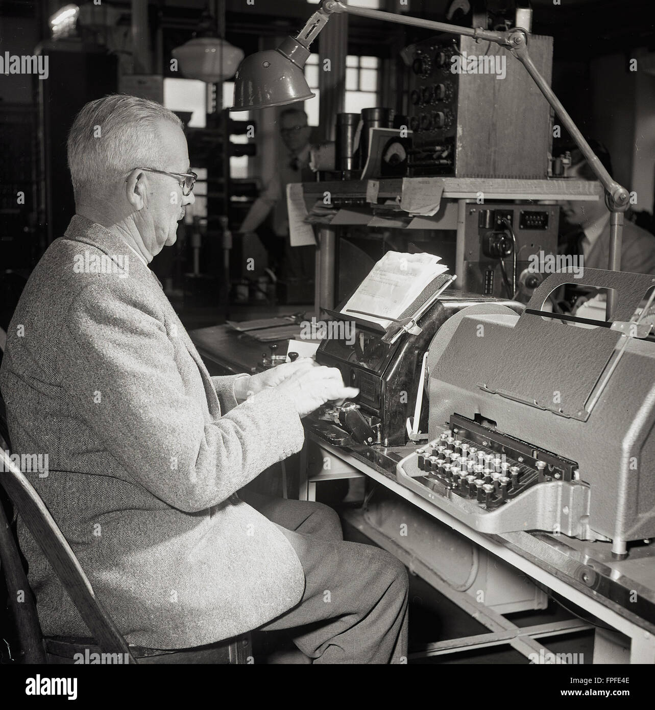1950s historical,  a male operator sitting at a machine sending a telex message from the Trans-Atlantic Cable Station in Waterville, Kerry, Ireland. In this era, the telex machine was a piece of  technology used for sending written messages either by electricity or radio signals and remained an important means of business communication until the development of the fax machine in the 1980s. Stock Photo