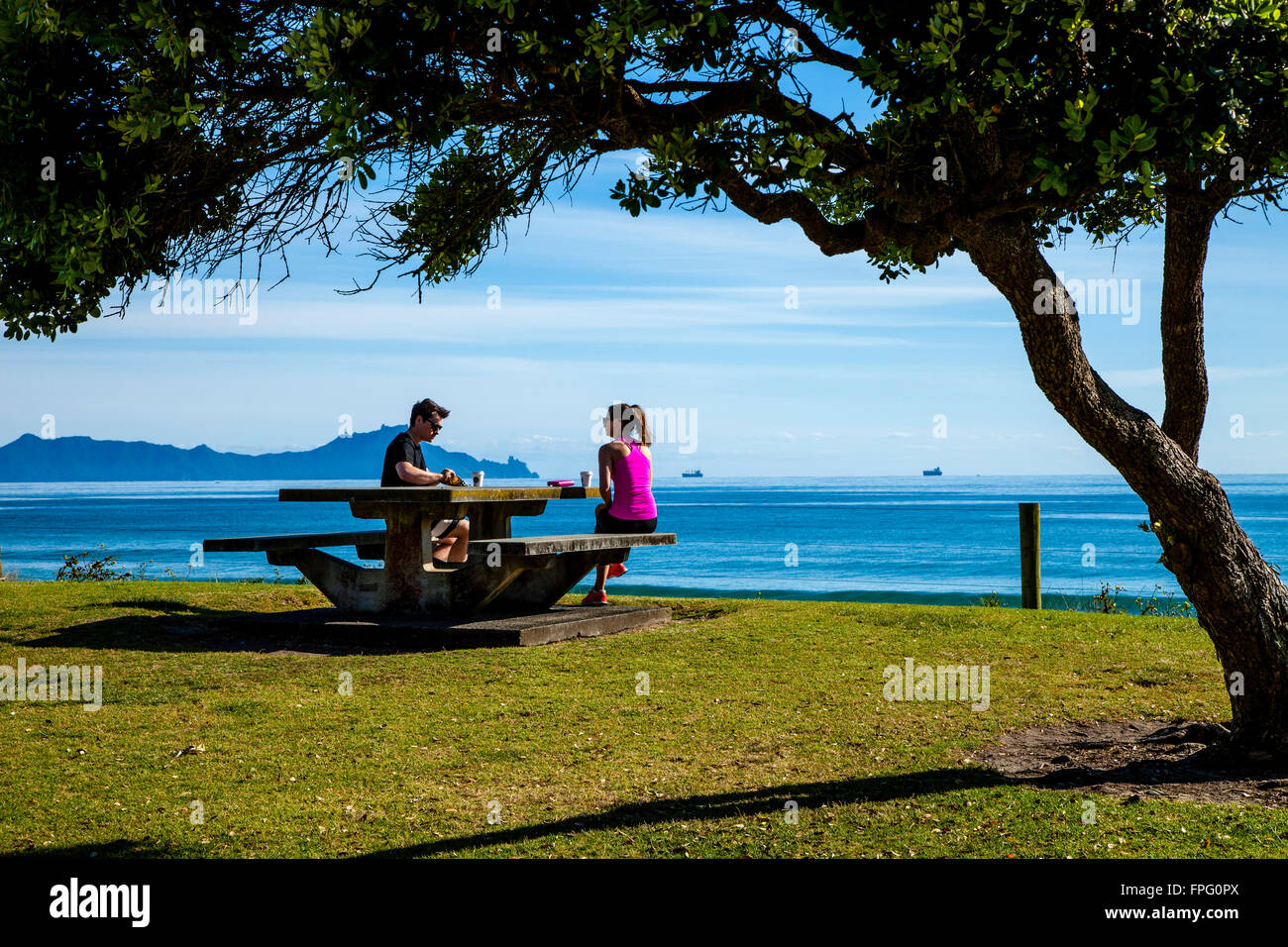 A Couple Drinking Coffee At A Picnic Table In Waipu Cove, Waipu, Northland, New Zealand Stock Photo