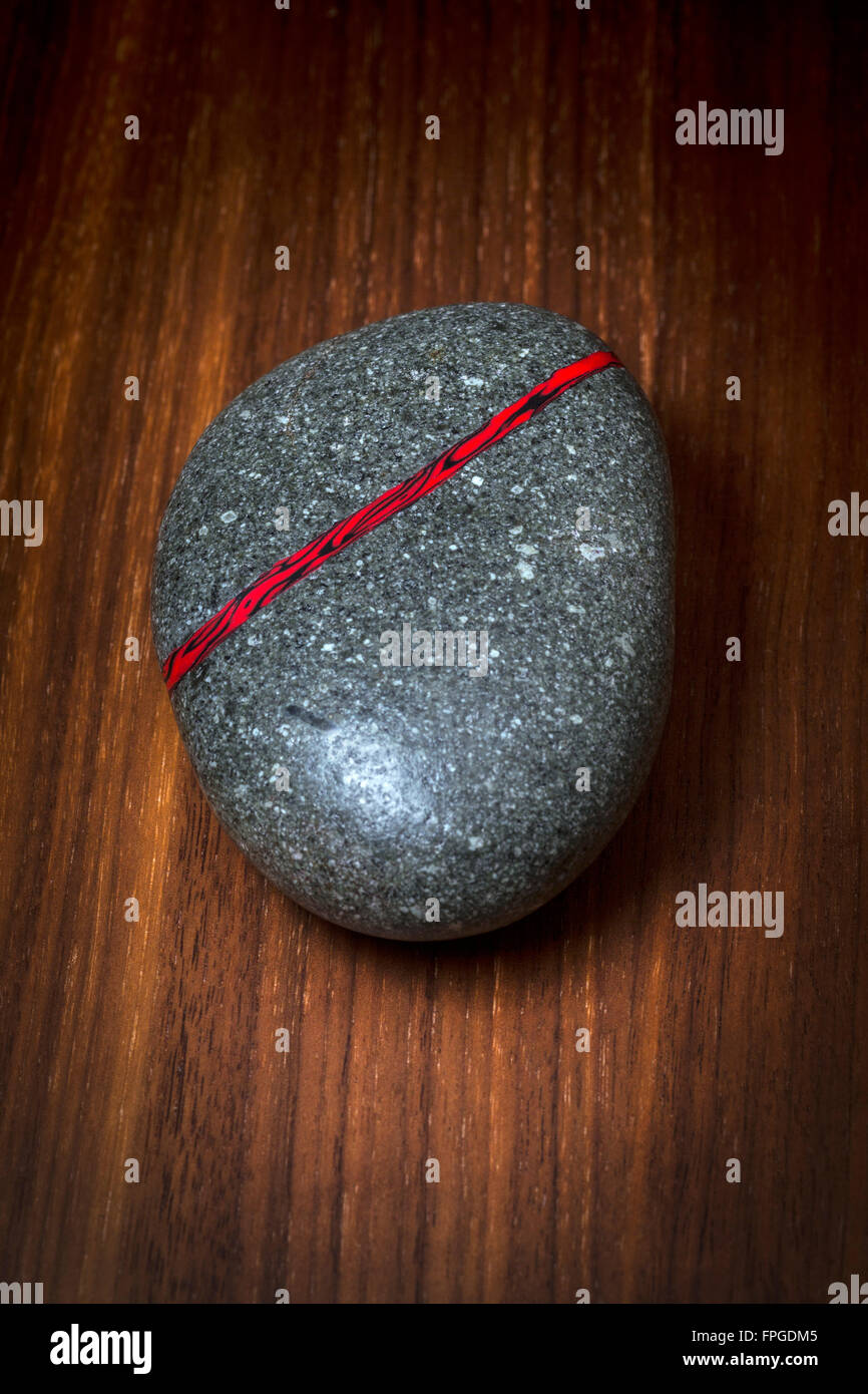 Natural pebble with an inlay of black and red resin vein. An original creation photographed in the studio on a walnut plank. Stock Photo