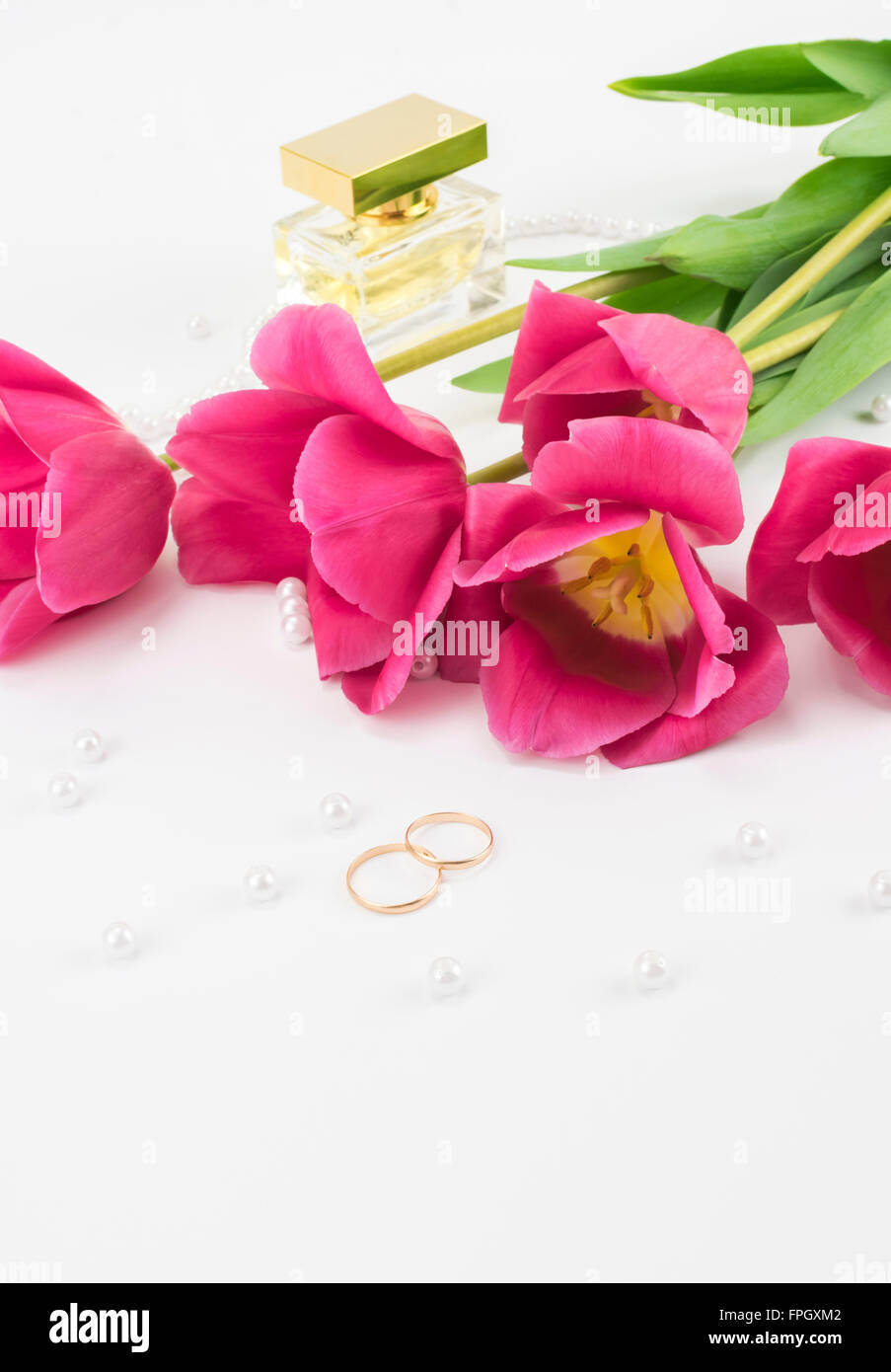 bouquet of red tulips, wedding rings, perfume and bead lying on a white background Stock Photo