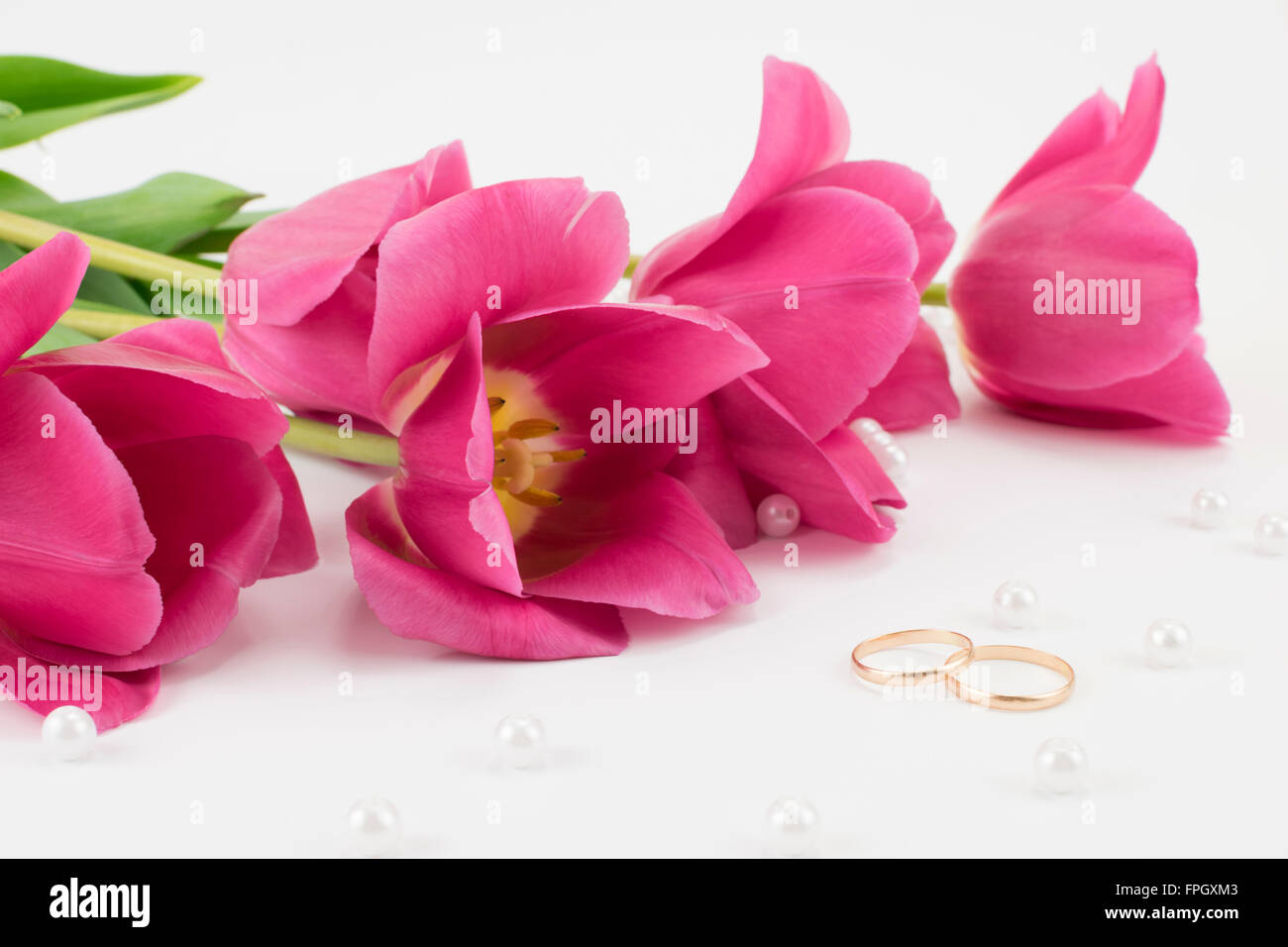 bouquet of red tulips, wedding rings, perfume and bead lying Stock Photo