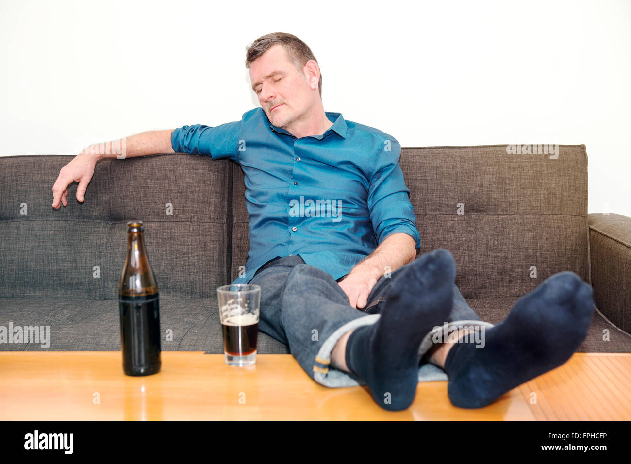 mature man sleeping on couch with a bottle of beer on the table Stock Photo